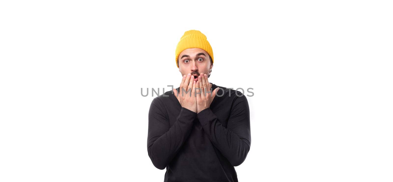 surprised handsome young 30 year old guy dressed in a black jacket and a yellow hat on a white background with copy space by TRMK