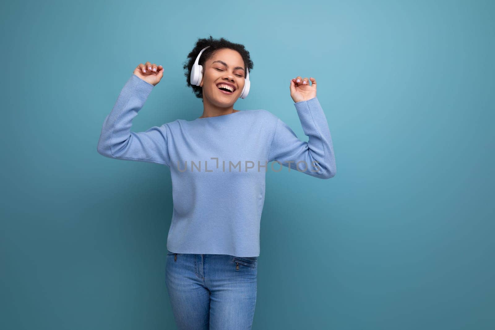 energetic 20s young afro brunette woman with wireless headphones on studio background with copy space.