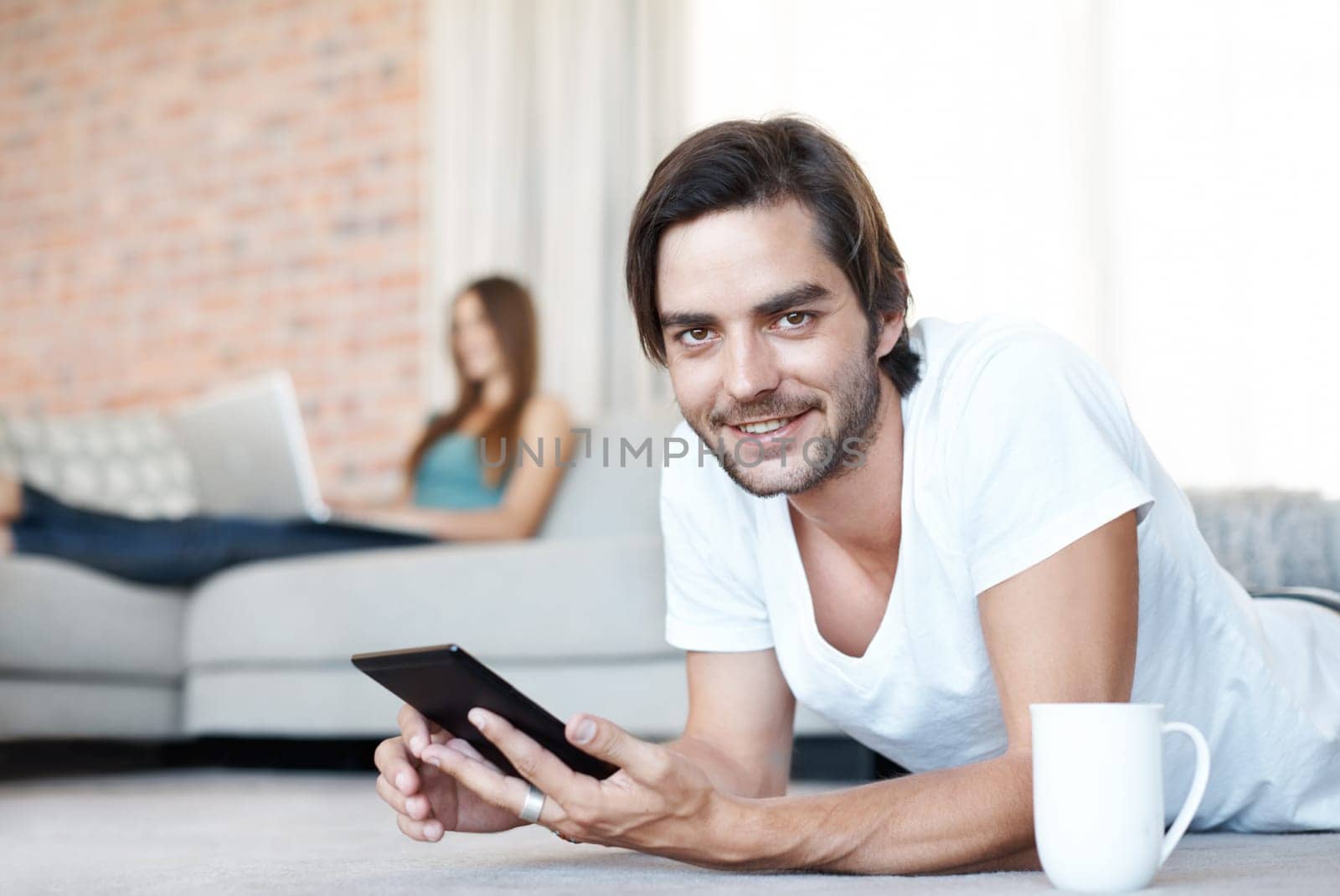 Technology makes me happy. Attractive young man lounging at home using his tablet. by YuriArcurs