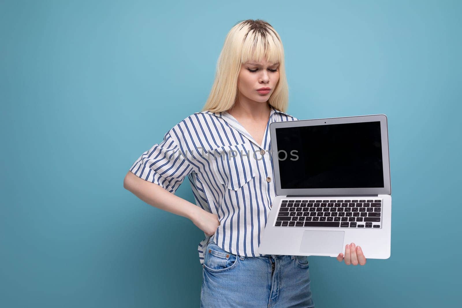 successful freelance blond young woman in striped shirt showing advertisement on laptop in studio background.