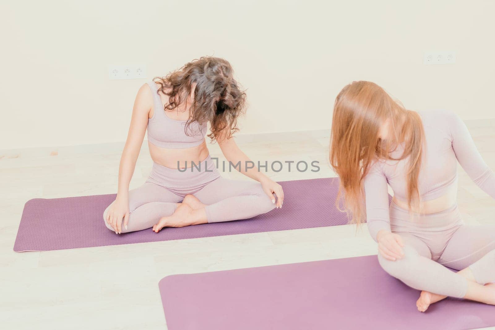 Young woman with long hair in white swimsuit and boho style braclets practicing outdoors on yoga mat by the sea on a sunset. Women's yoga fitness routine. Healthy lifestyle, harmony and meditation