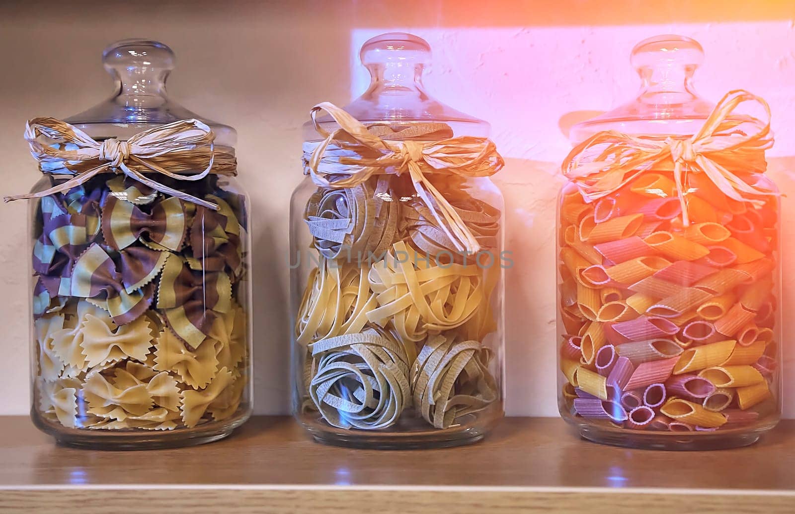 Colored pasta in glass jars. Vegan source of protein and energy resources. Rustic wooden kitchen table background.