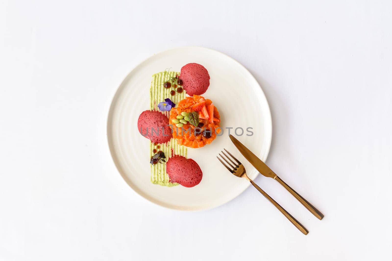 Salmon tartare with strawberries, beans and sauce on a white plate on a white background