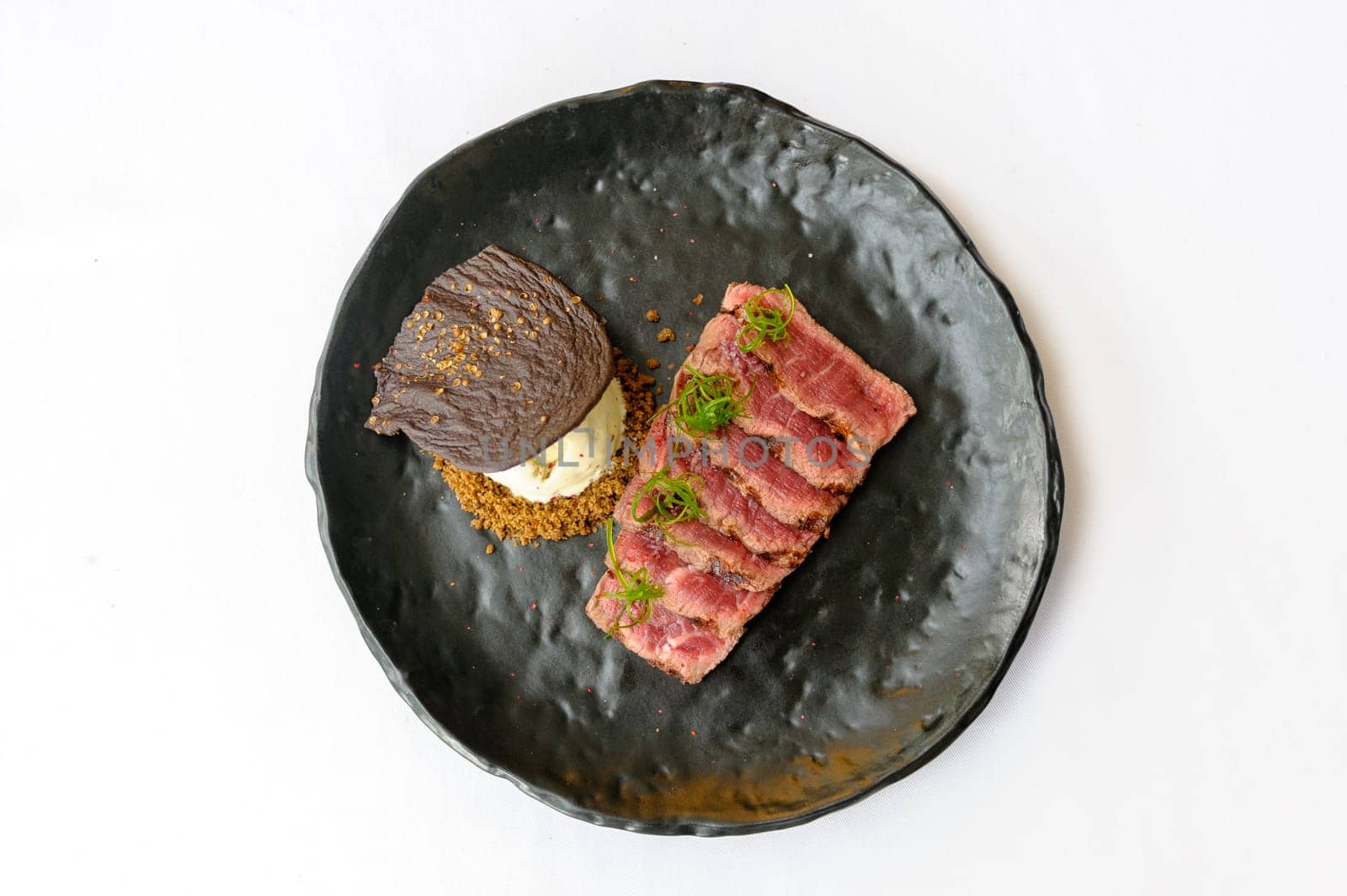 Exquisite serving of medium roasted beef slices on a black plate on a white background