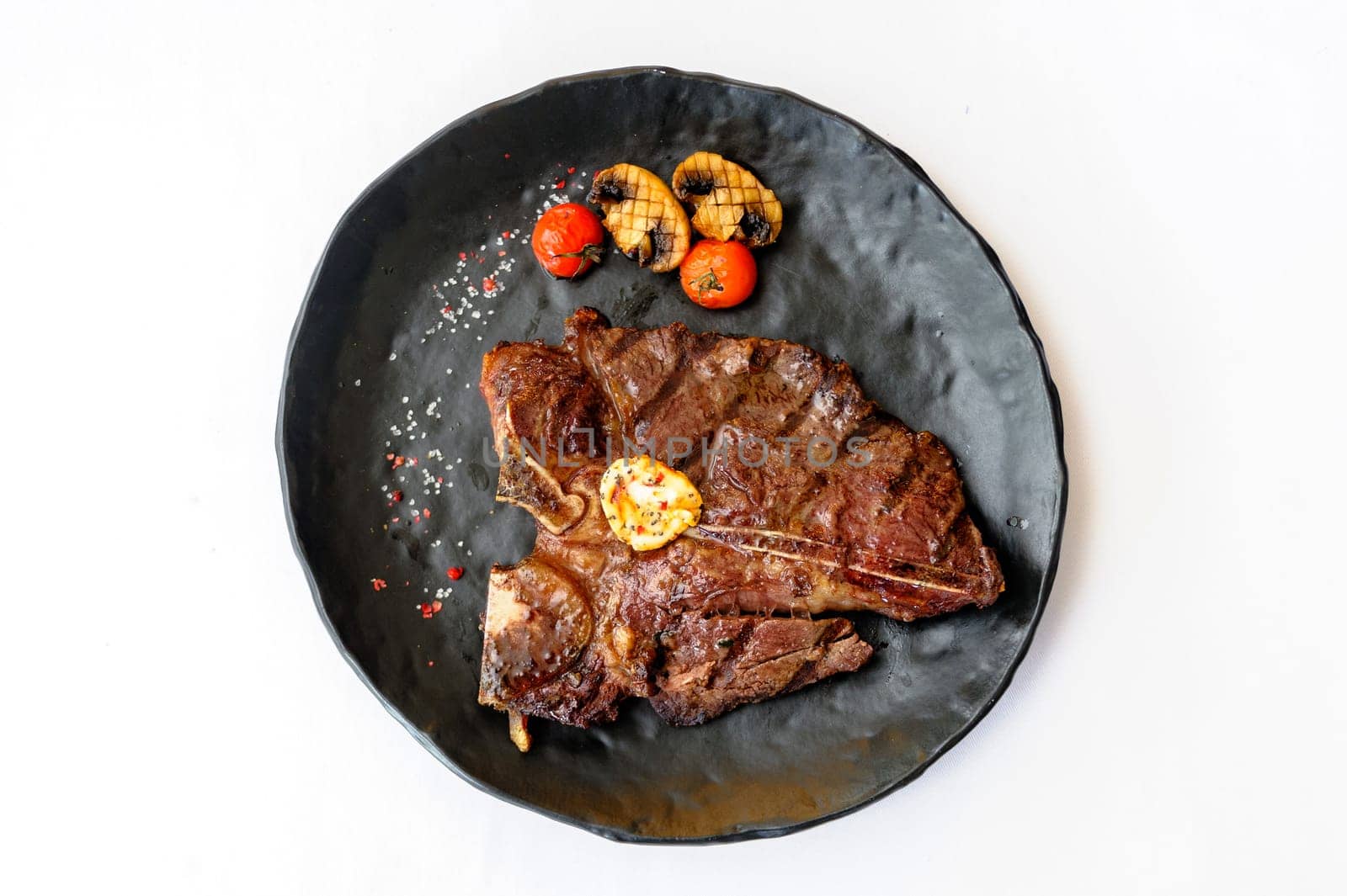 Exquisite serving of bone-in beef steak on a black plate on a white background