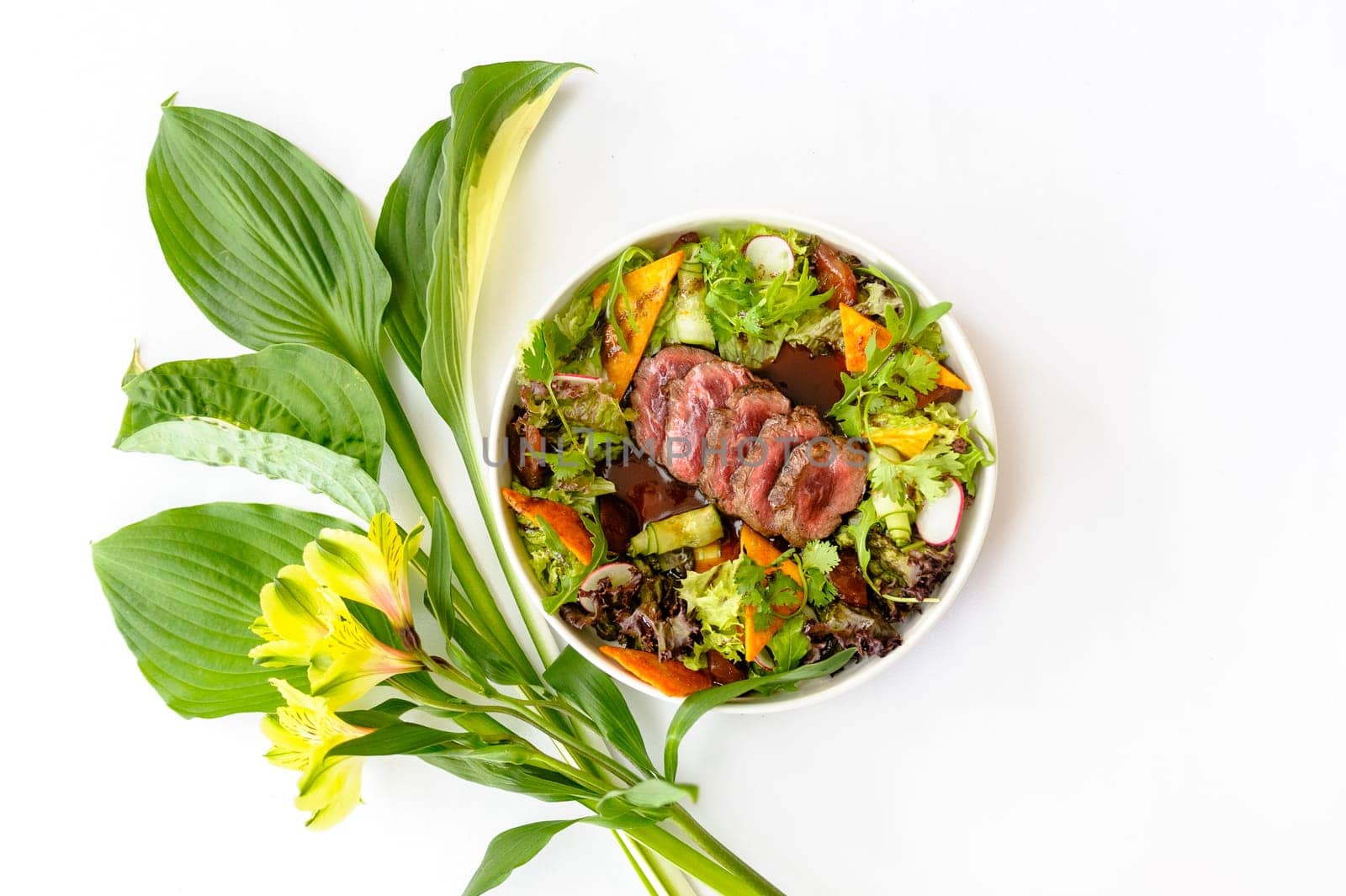 Salad with medium roasted beef and greens on a white plate decorated with bright flowers on a white background