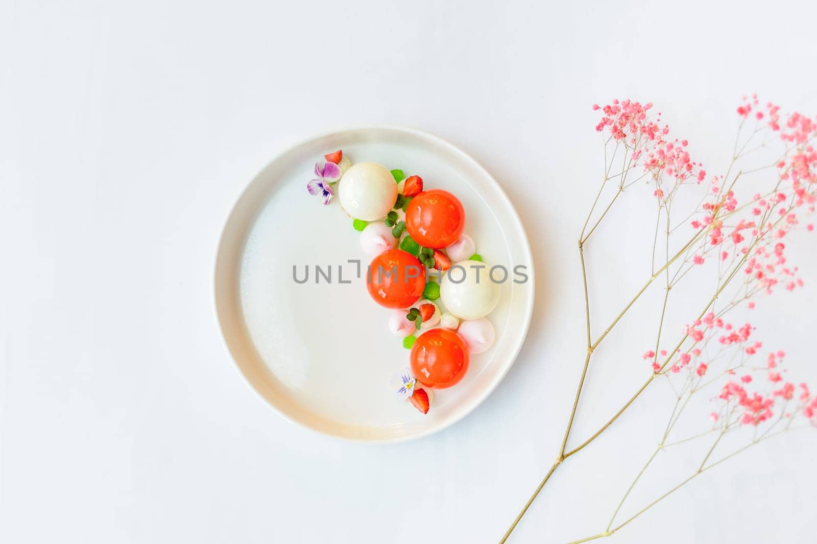 Bright dessert with strawberries and mousse decorated with flowers on a white plate