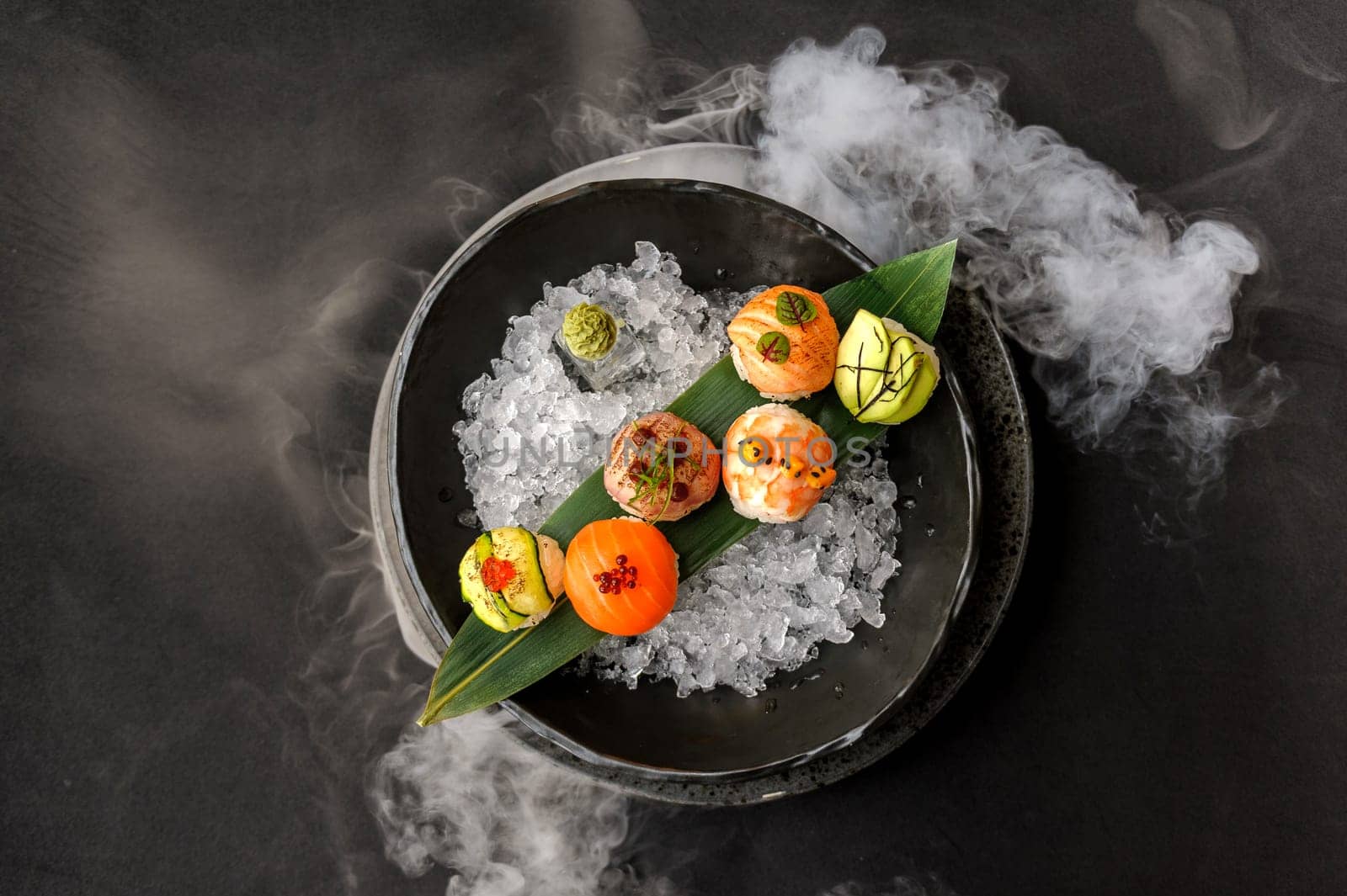 Temari sushi on a black plate with ice and bamboo leaf