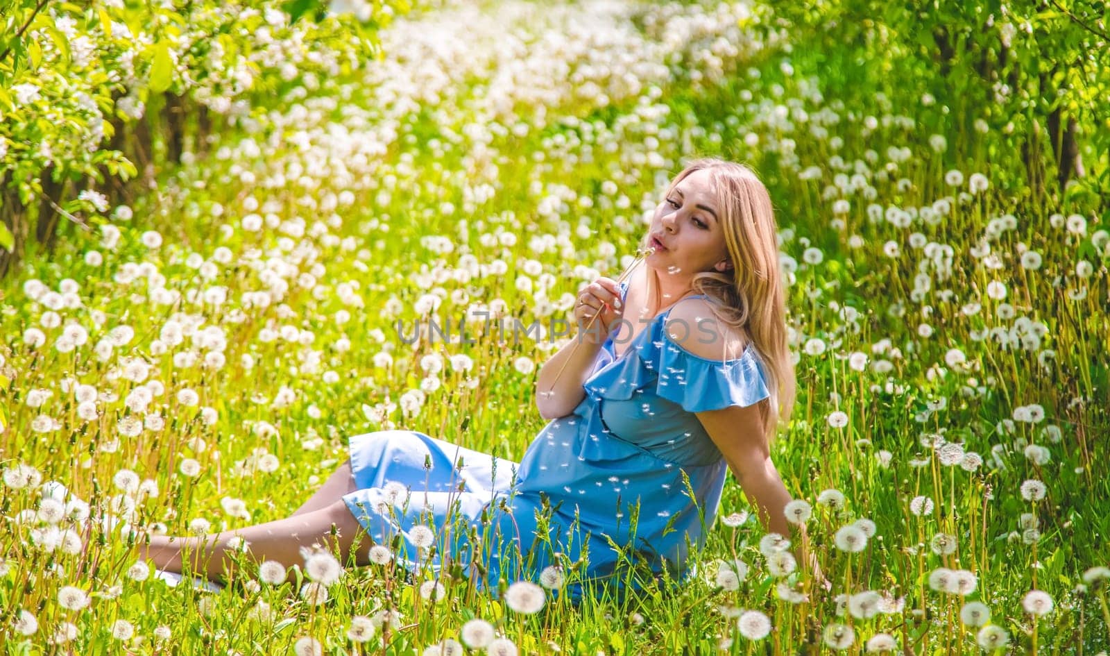 Pregnant woman with dandelions in the garden. Selective focus. Nature.