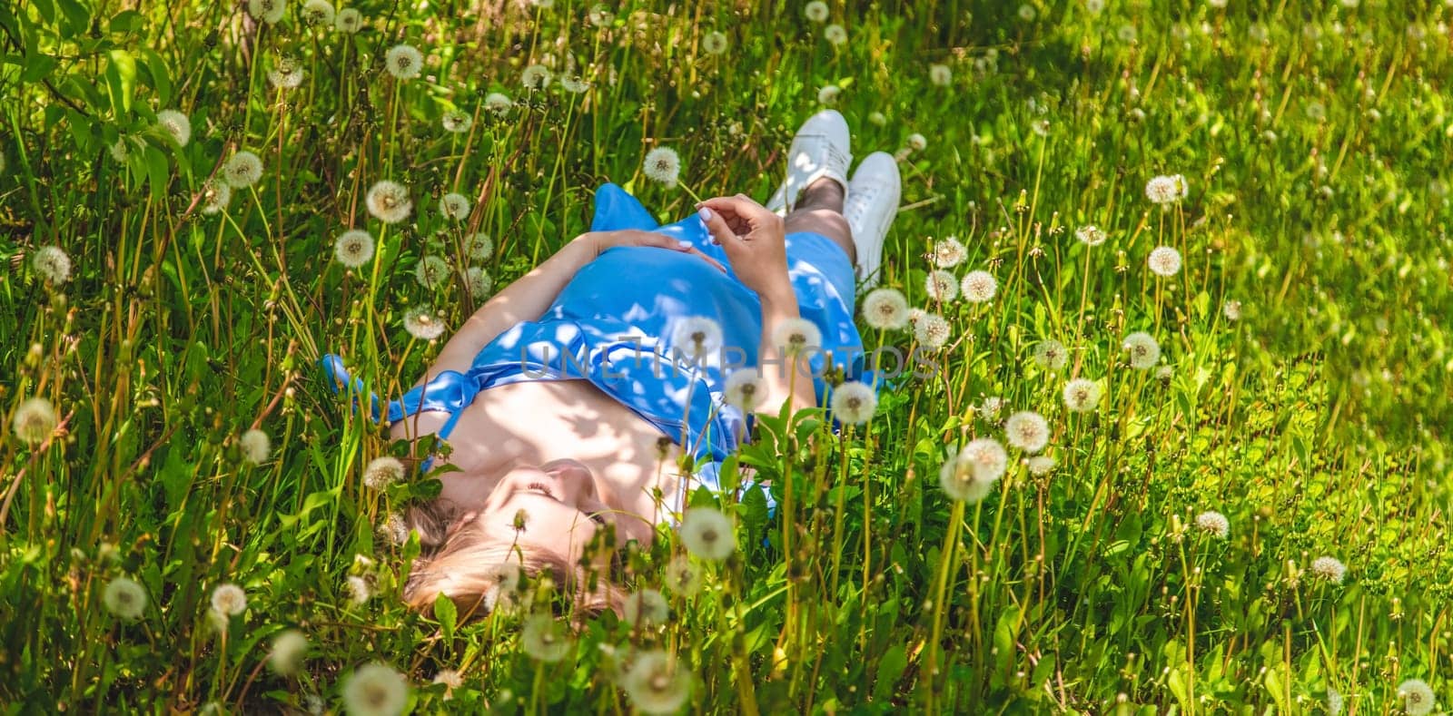 Pregnant woman with dandelions in the garden. Selective focus. Nature.