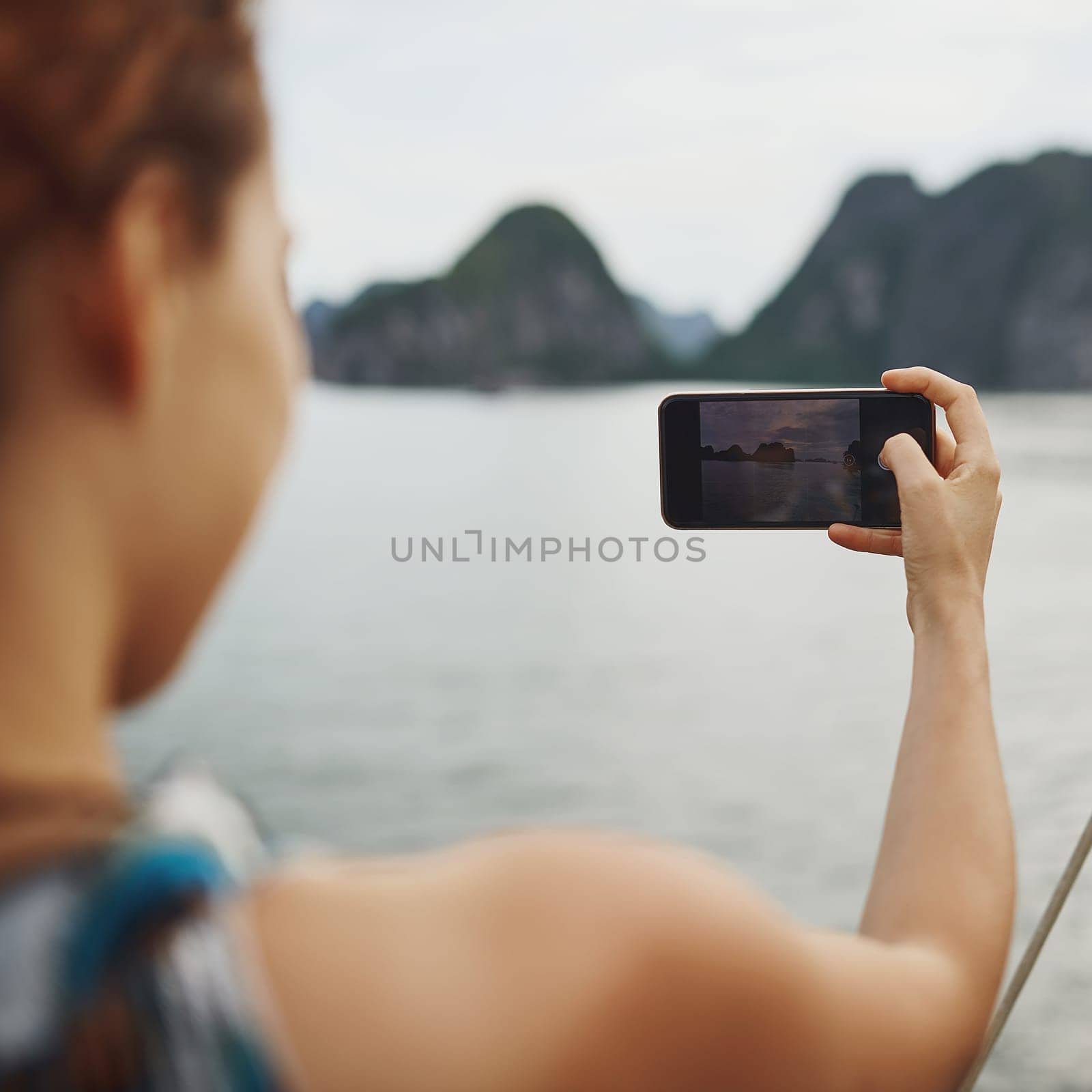 Something to look back on and smile. a young woman taking pictures of a river in Vietnam with her smartphone. by YuriArcurs