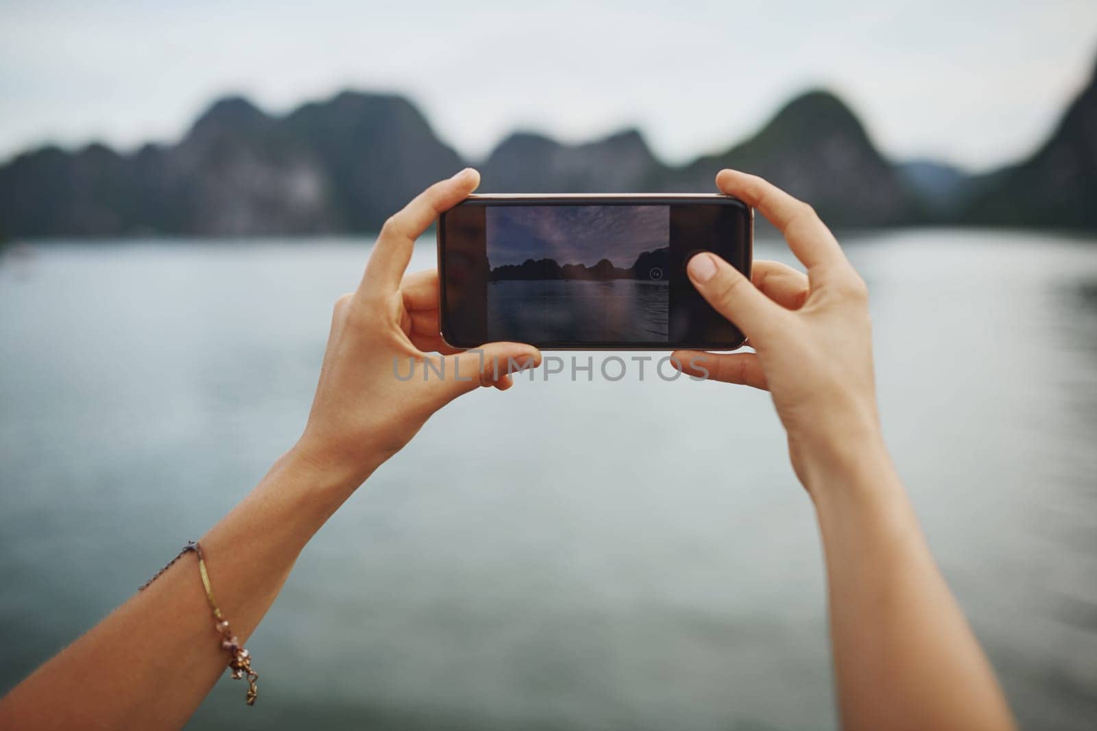 The more you travel the more memories you make. a young woman taking pictures of a river in Vietnam with her smartphone. by YuriArcurs
