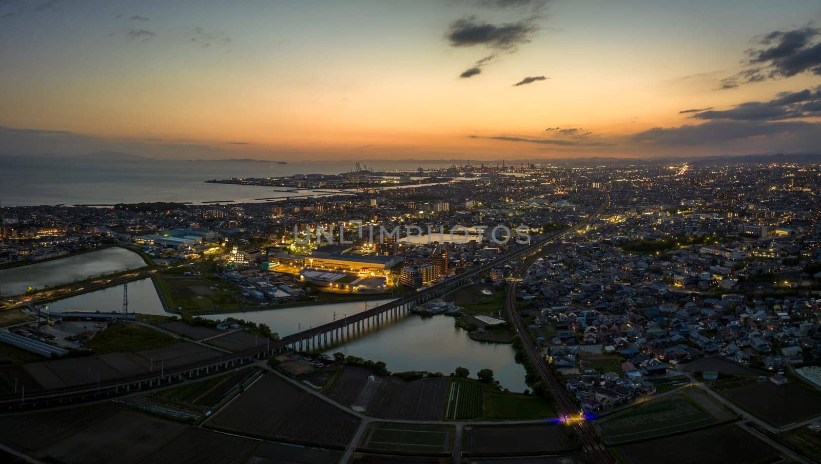 Aerial view of train tracks over pond with sunset glow in sky as city lights up. High quality photo