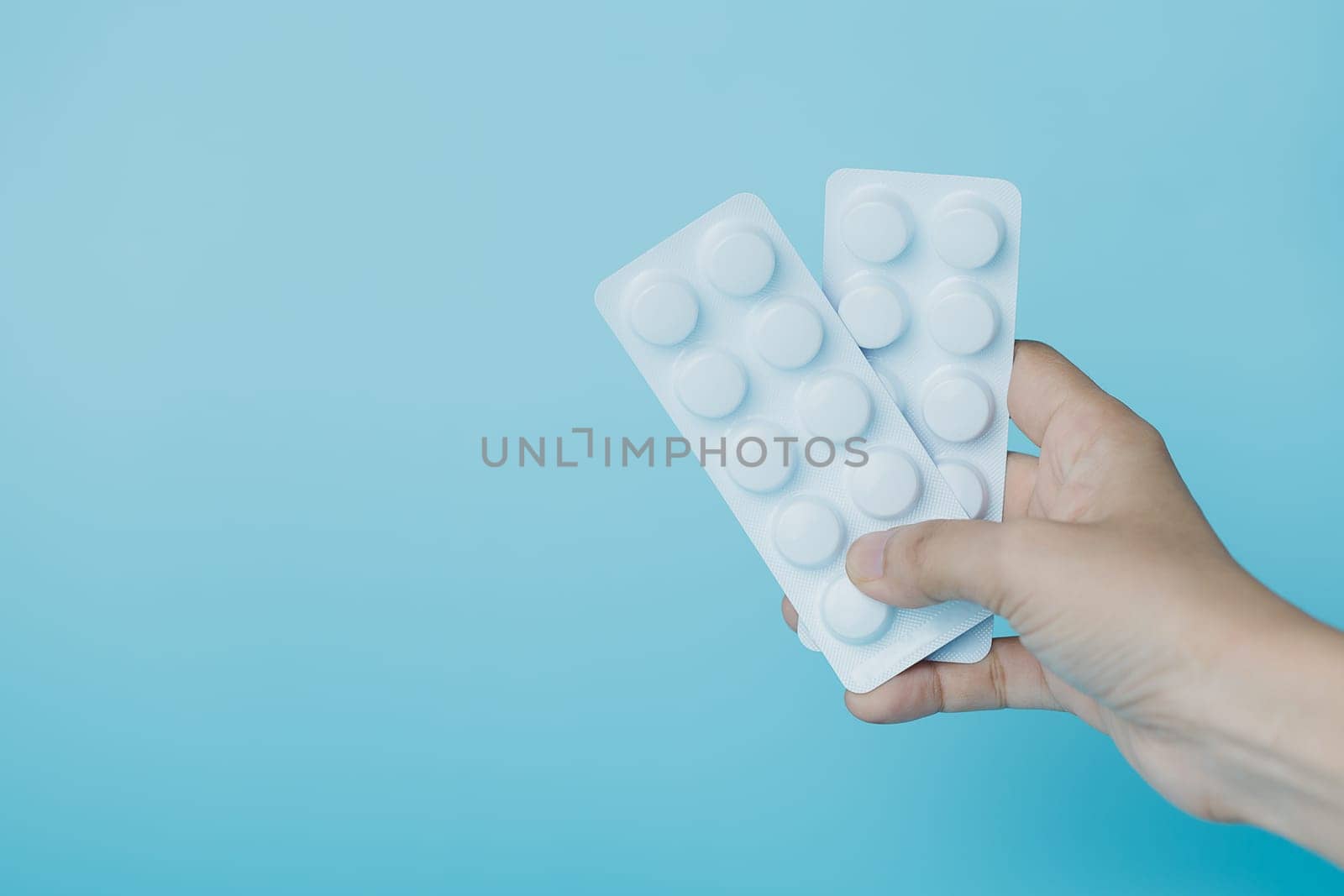 Hand holding a blister pack of medicine pill on blue background for medical and healthcare concept