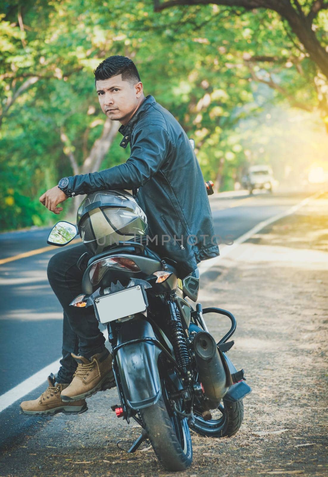 Portrait of biker in jacket sitting on his motorcycle at the side of the road. Latin motorcyclist sitting on his motorbike near a road by isaiphoto