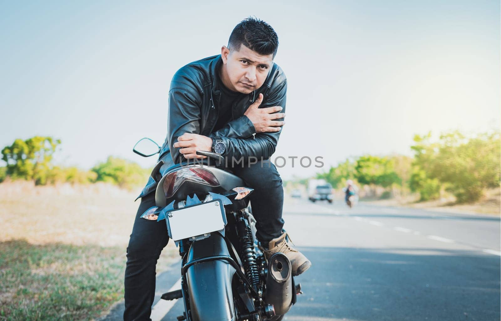 Portrait of handsome biker on his motorbike looking at camera outdoors. Handsome motorcyclist in jacket sitting on his motorcycle at the side of the road