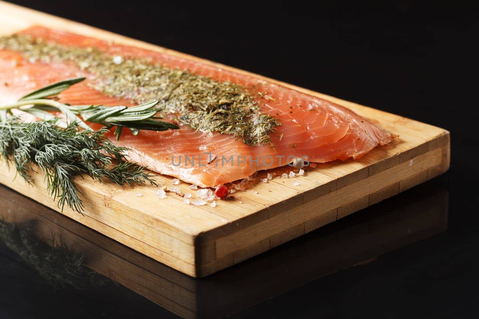 Salted fish fillet with spices and herbs:dill and rosemary on a wooden board on a black background. by lara29