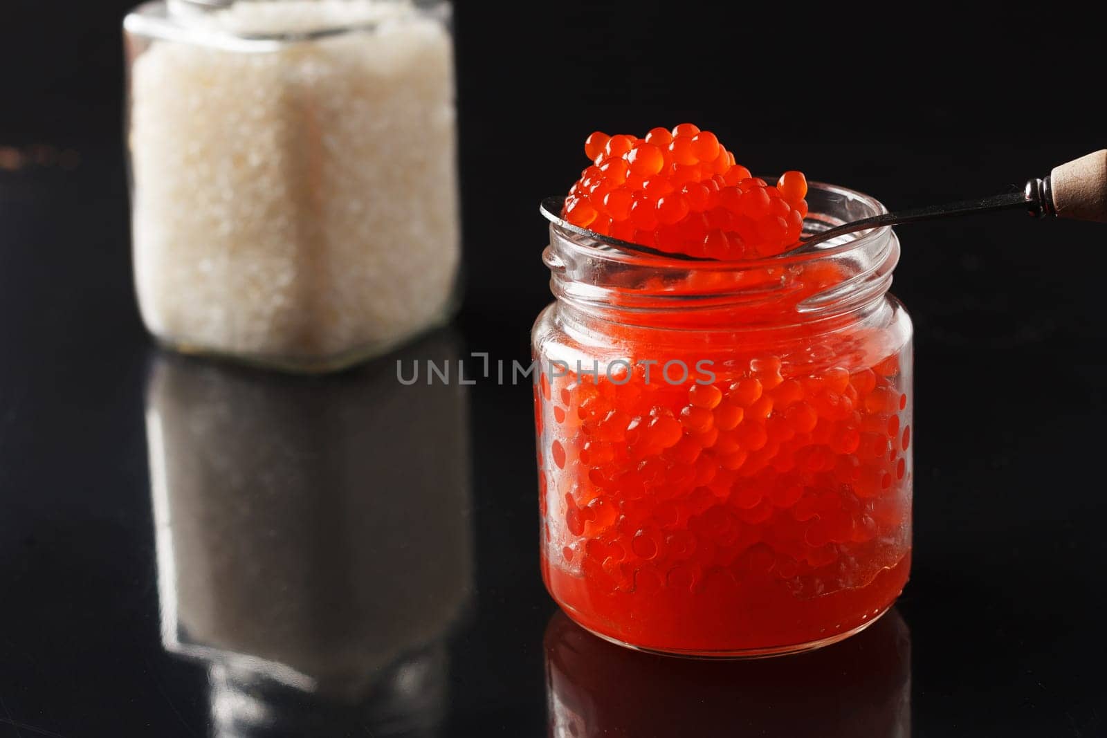 delicious red caviar in a glass jar and a jar of salt on a black background. by lara29