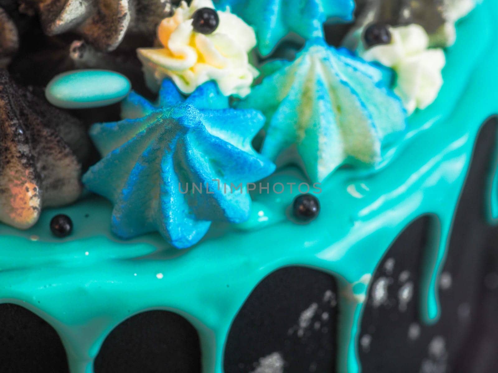 frosted black painted cup cake with blue turquoise dripping and colored handmade meringue topping studio white isolated background