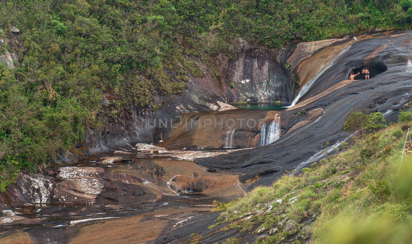 Long exposure shot of unrecognizable tourists taking photos for social media in the iconic spot of Caparao's valley with colorful water pools flowing over solid rock surrounded by jungle.