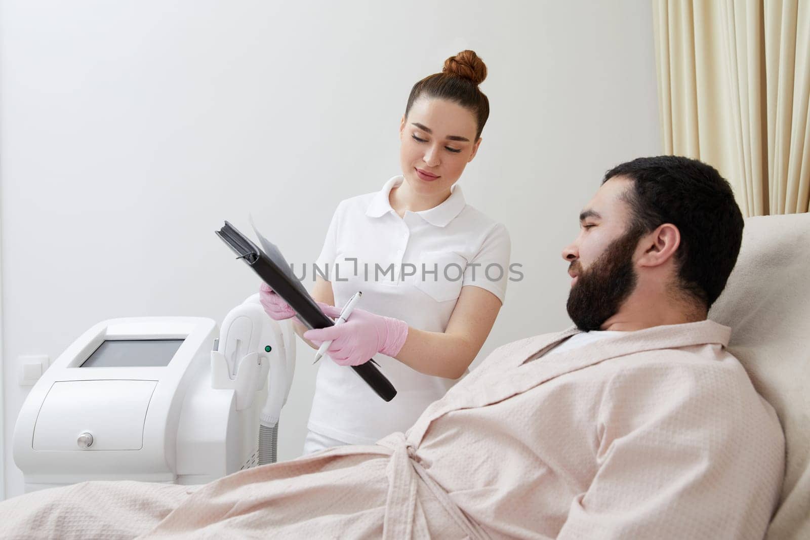 Professional cosmetician woman with papers talking to man before procedure in clinic of esthetic cosmetology by Mariakray
