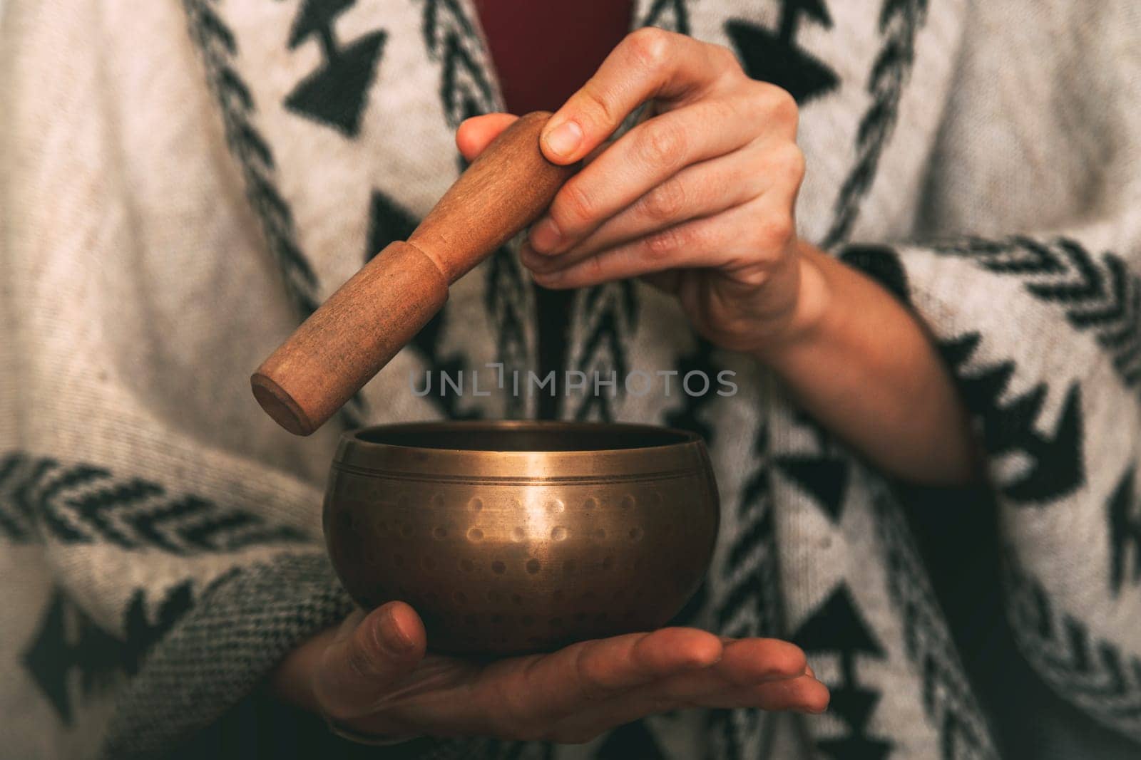hands of a woman using a golden tibetan bowl in a meditation dressed with a handmade poncho. background with copy space. concept meditation. horizontal image