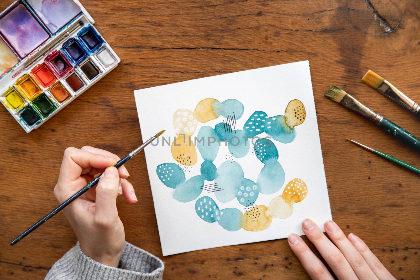 Unrecognizable young woman's hand painting an abstract watercolor art piece. Mix media art. Watercolour palette and paintbrush. Creativity and art concept.
