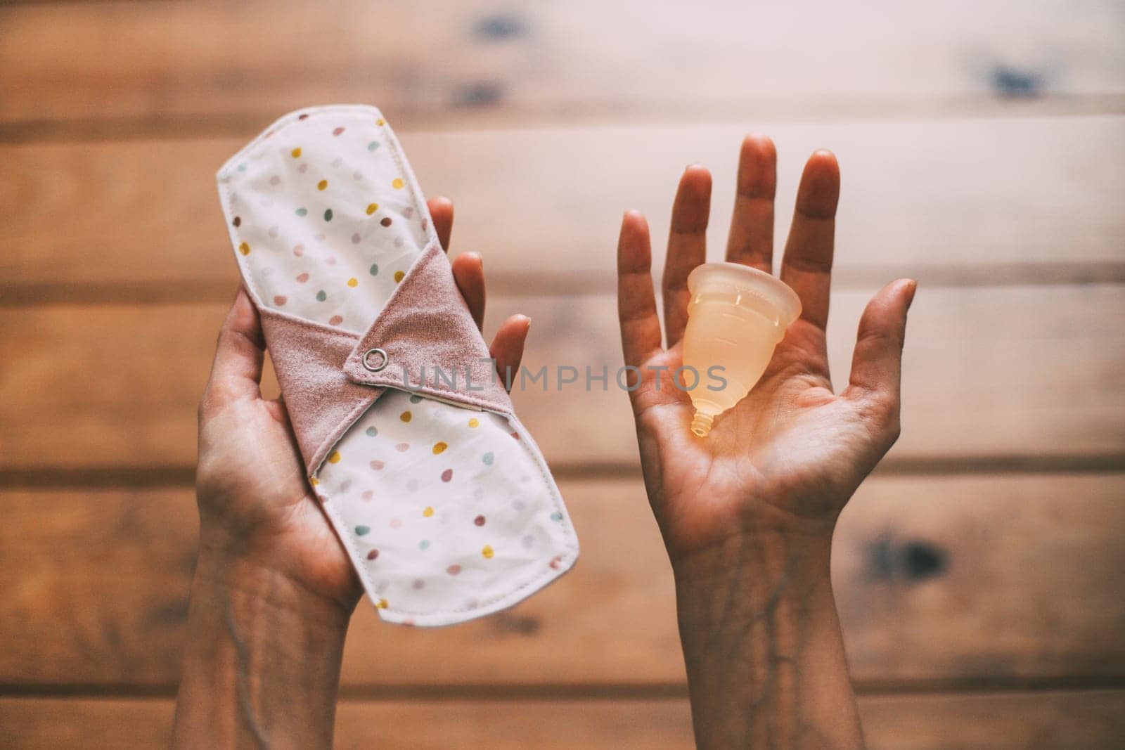 hands of a woman holding a reusable handmade cloth menstrual pad and a menstrual cup. feminine intimate hygiene concept. zero waste concept. environmental sustainability concept by Hoverstock