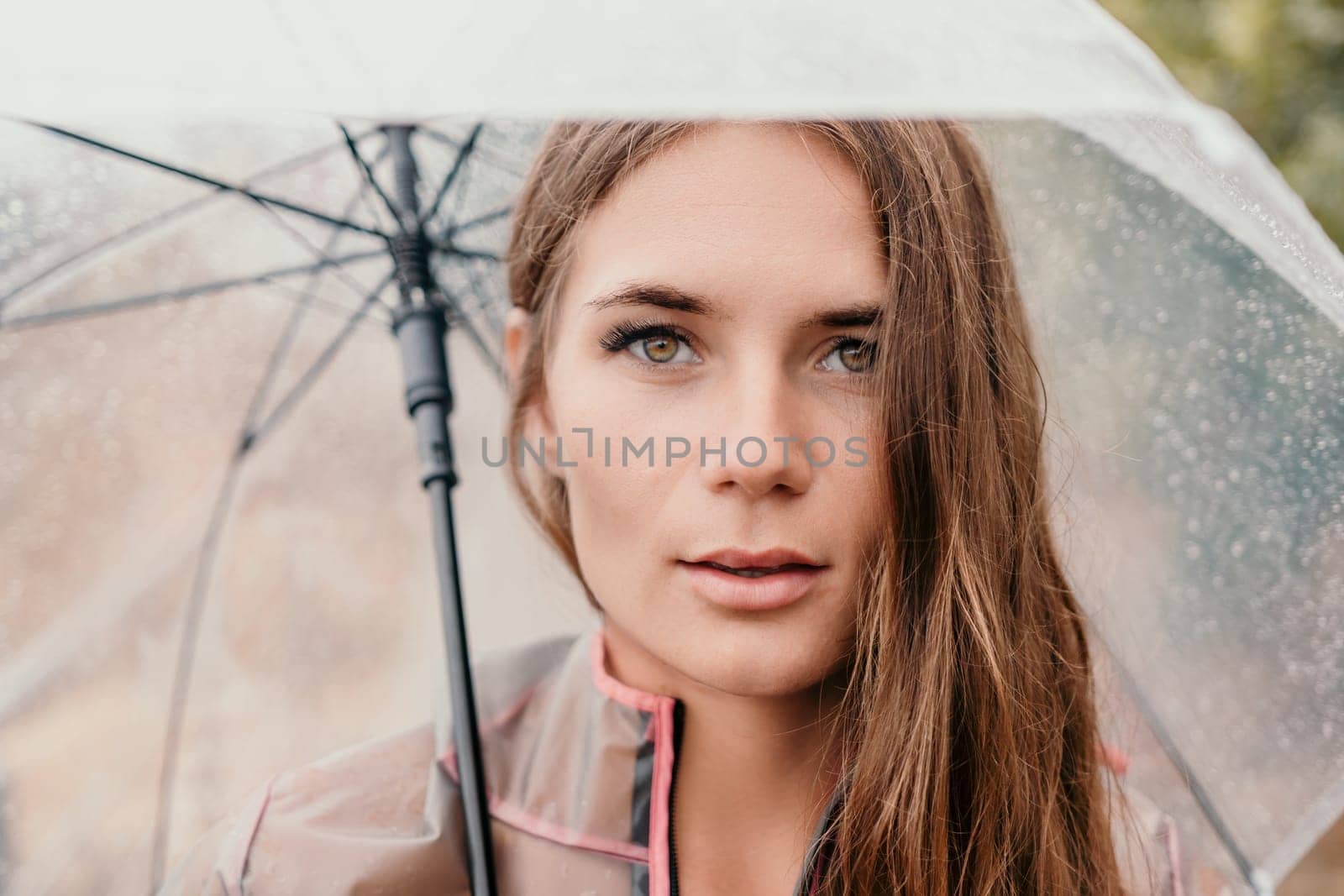 Woman rain park. Happy woman portrait wearing a raincoat with transparent umbrella outdoors on rainy day in park near sea. Girl on the nature on rainy overcast day