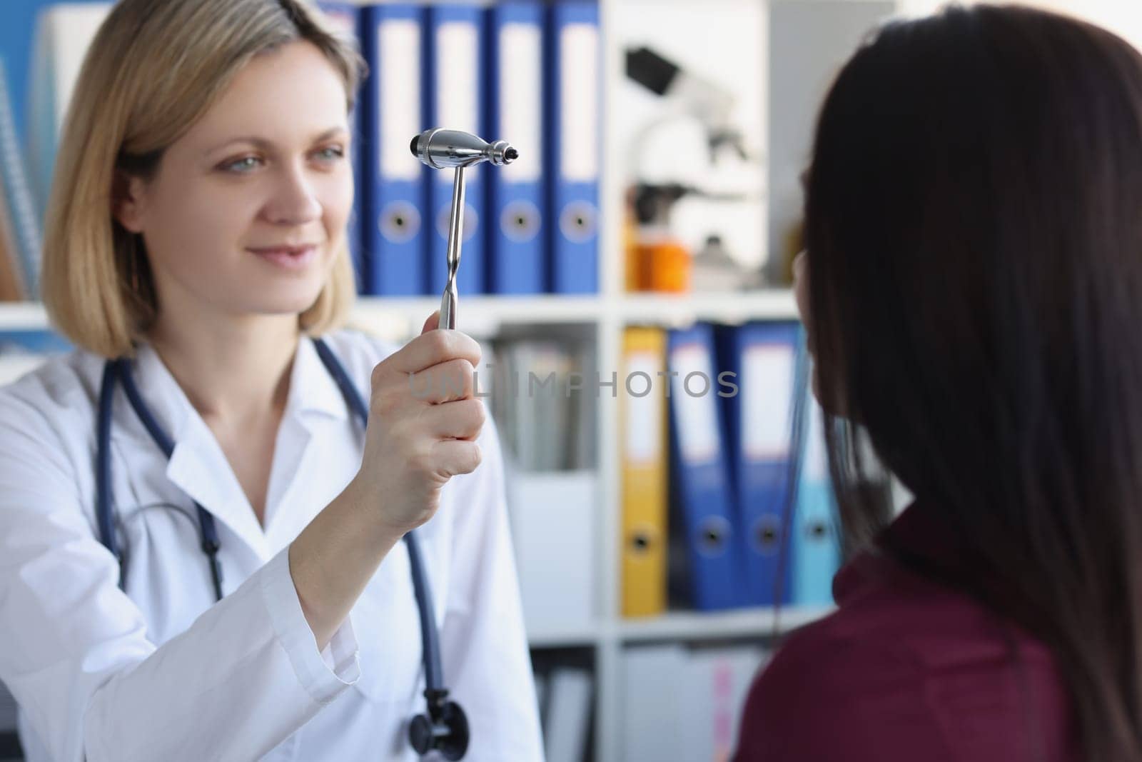 Female neurologist examines patient with hammer in private clinic. Neurologist consultation and diagnosis of diseases concept
