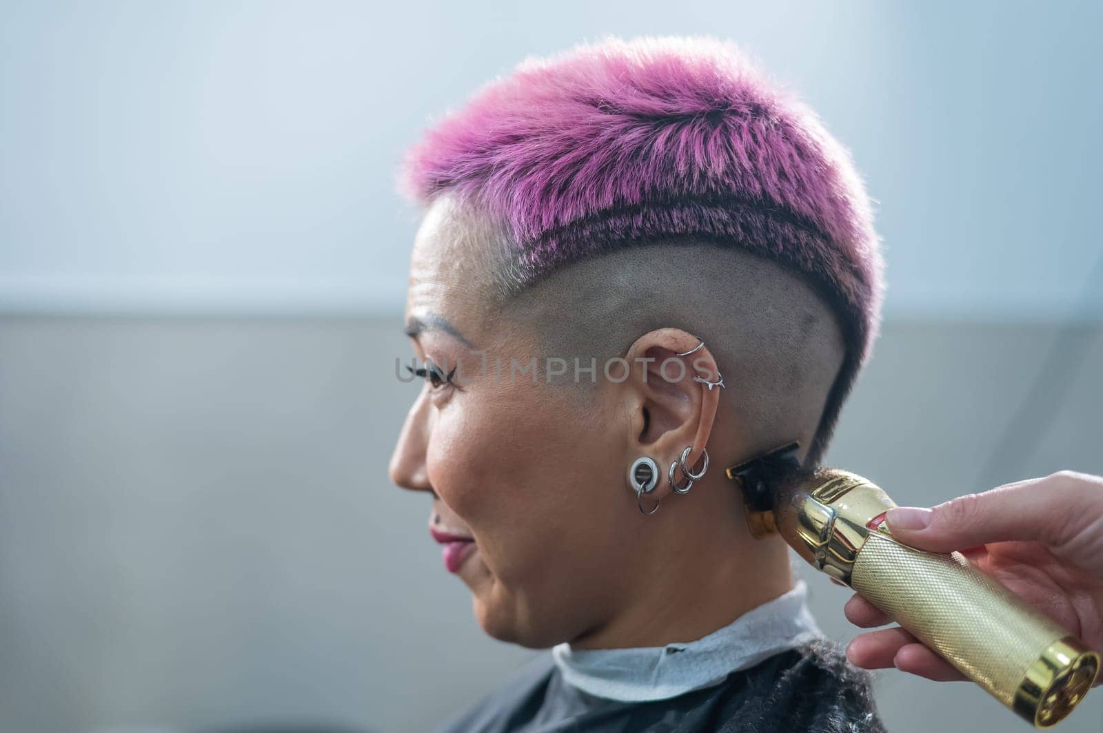 The hairdresser shaves the temple of a female client. Asian woman with short pink hair in barbershop. by mrwed54