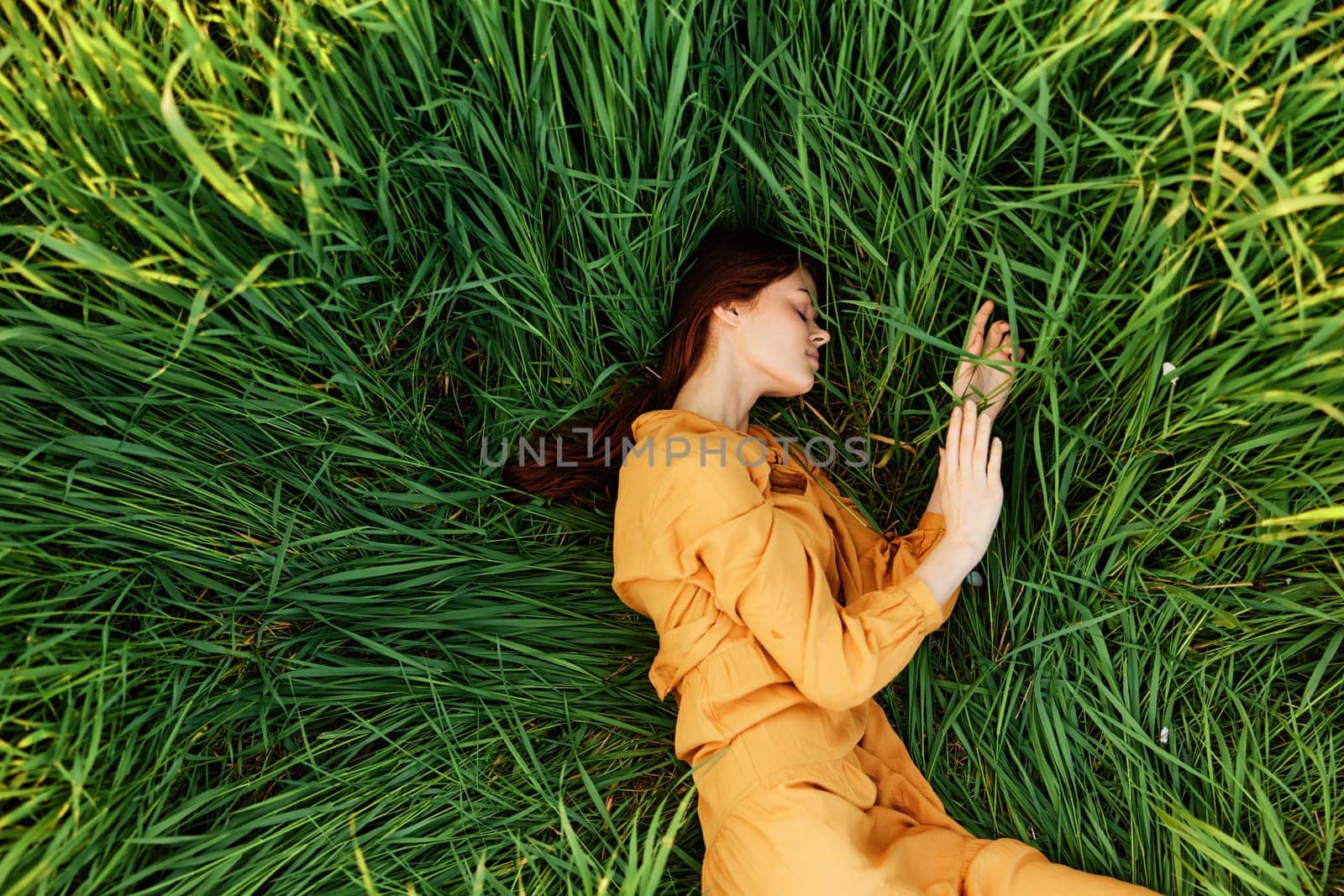 a relaxed woman enjoys summer lying in the tall green grass with her eyes closed. Photo taken from above by Vichizh