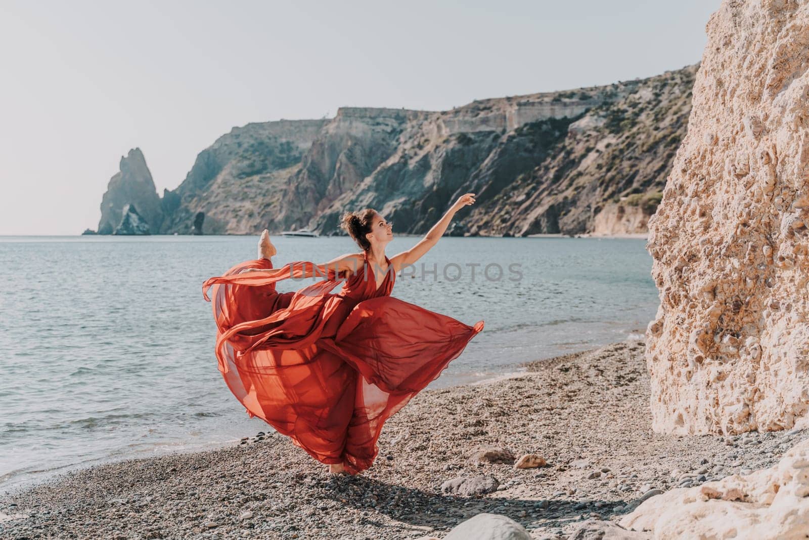 Woman red dress sea. Female dancer in a long red dress posing on a beach with rocks on sunny day. Girl on the nature on blue sky background. by Matiunina