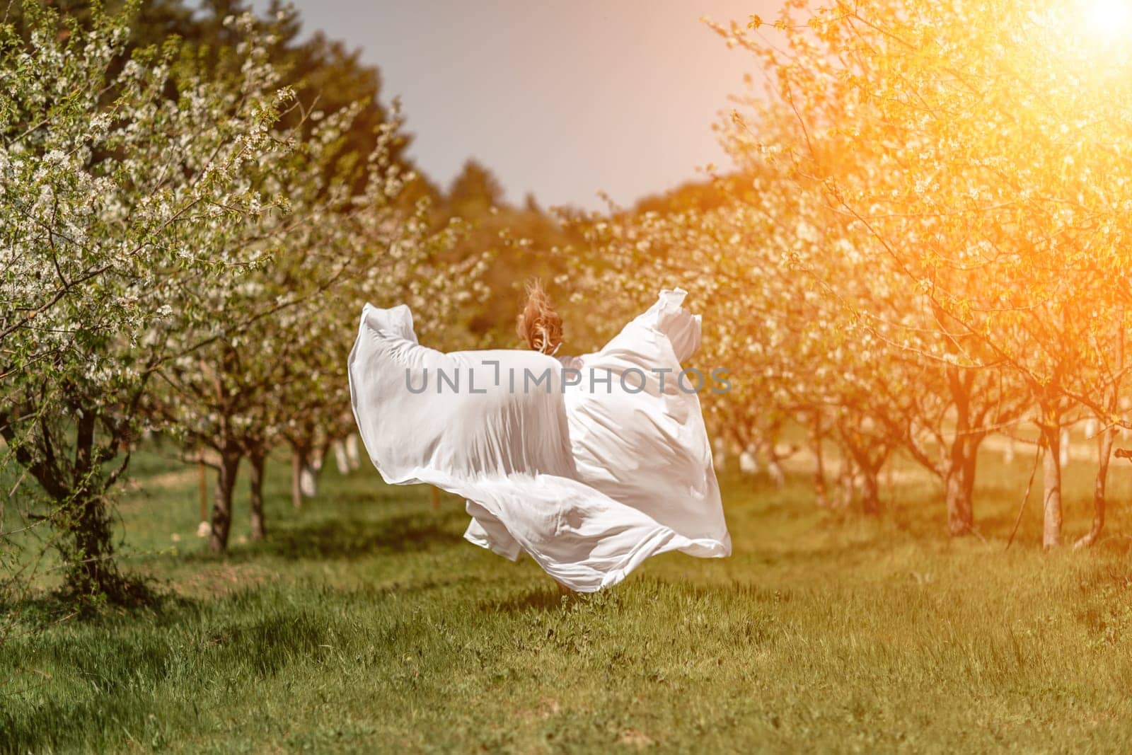 Woman white dress park. A woman in a white dress runs through a blossoming cherry orchard. The long dress flies to the sides, the bride runs rejoicing in life