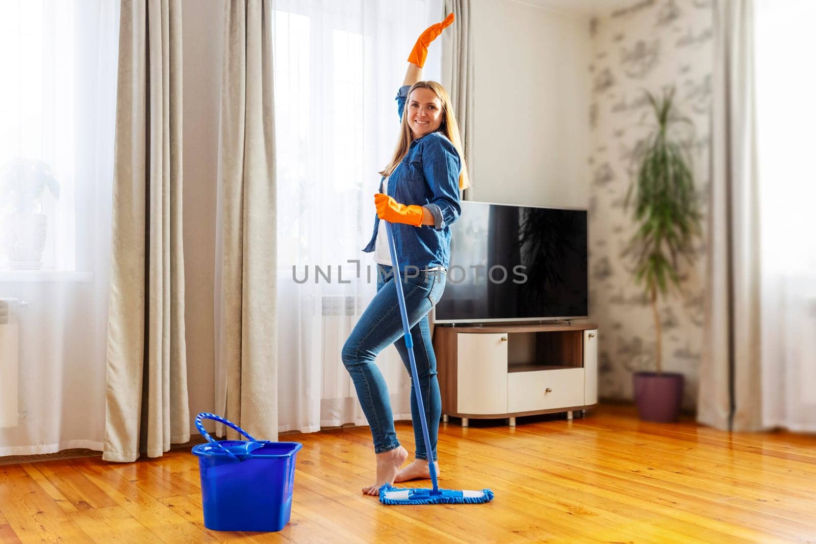 Funny happy young woman with mop singing, dancing and having fun while cleaning floor. Housewife enjoying domestic chores, doing home cleanup creatively
