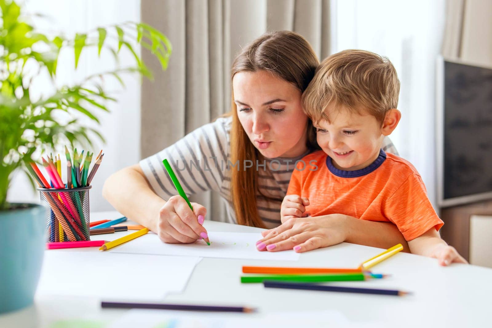 Mother and child drawing with pencils sitting at the desk at home by andreyz