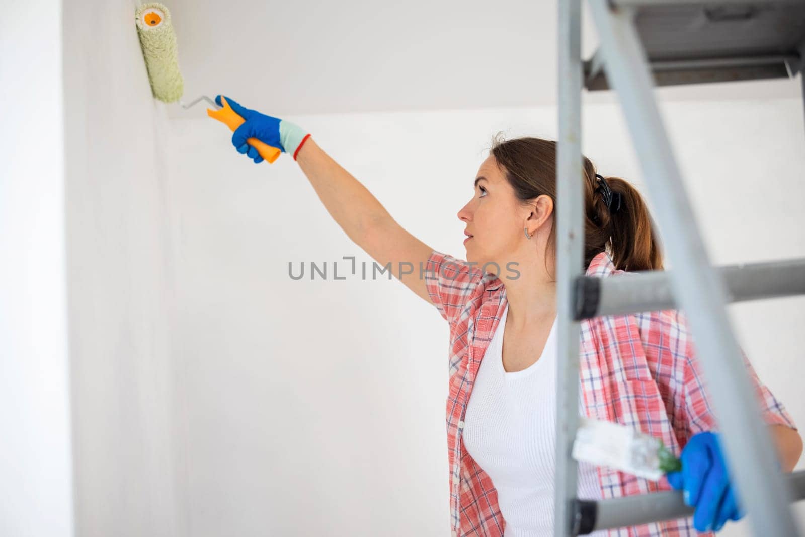 Happy woman with roller painting wall in her new apartment. Renovation, redecoration and repair concept