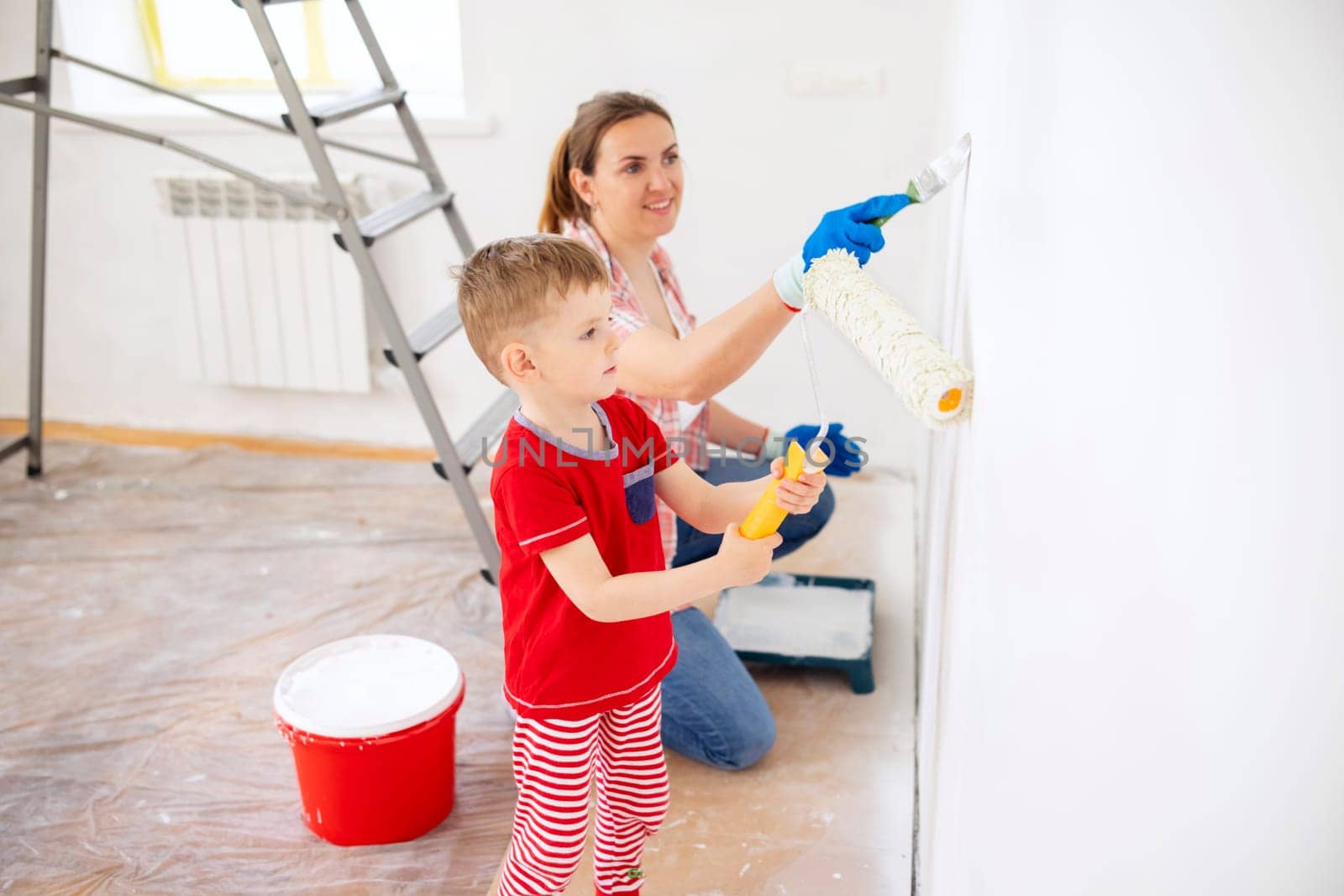 Happy family mother and child son paint the wall with paint using roller and brush. Repair in the apartment