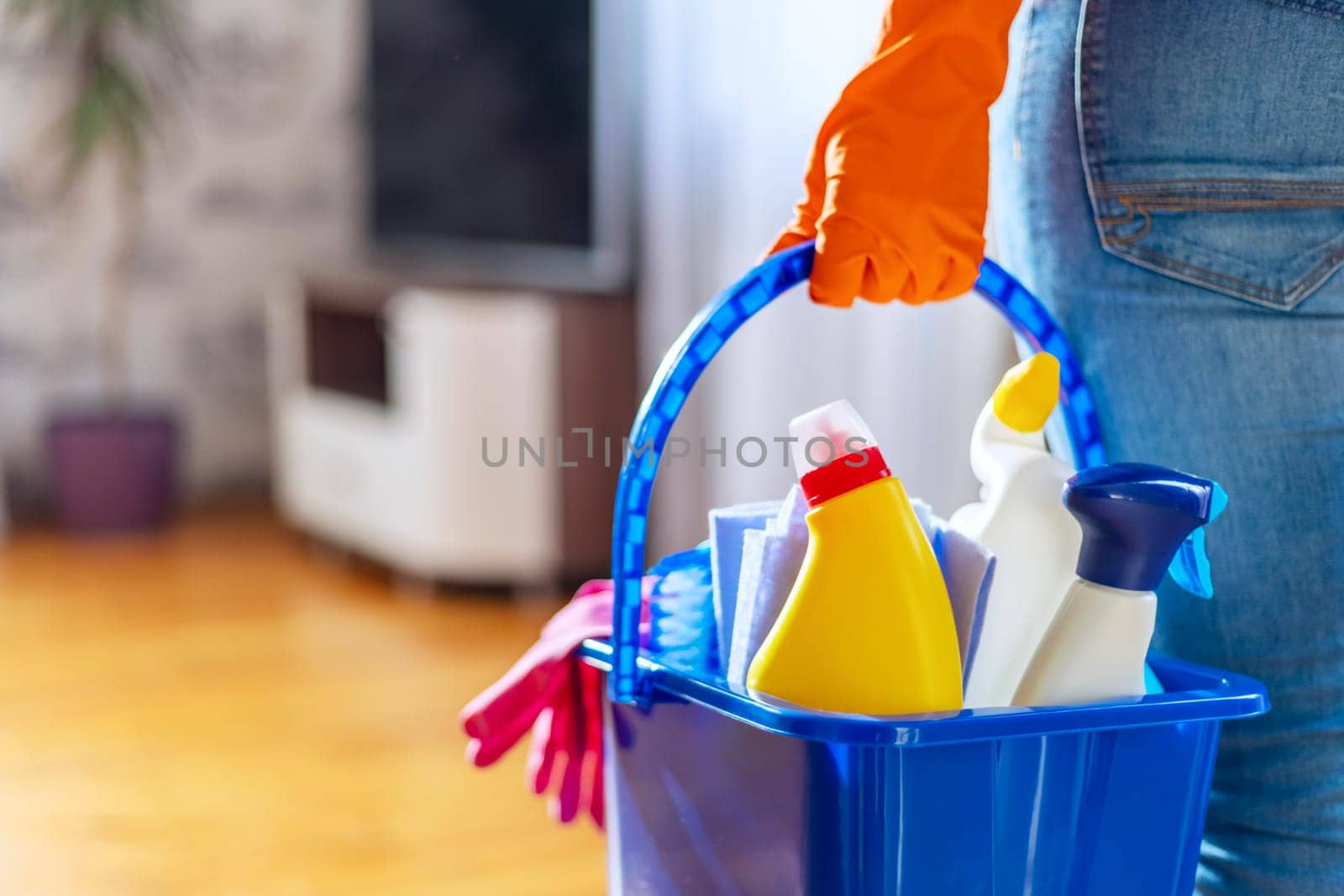 Woman in rubber gloves with bucket of cleaning supplies ready to clean up her apartment. Housewife has many household chores, domestic work and professional cleaning service. Low depth of field