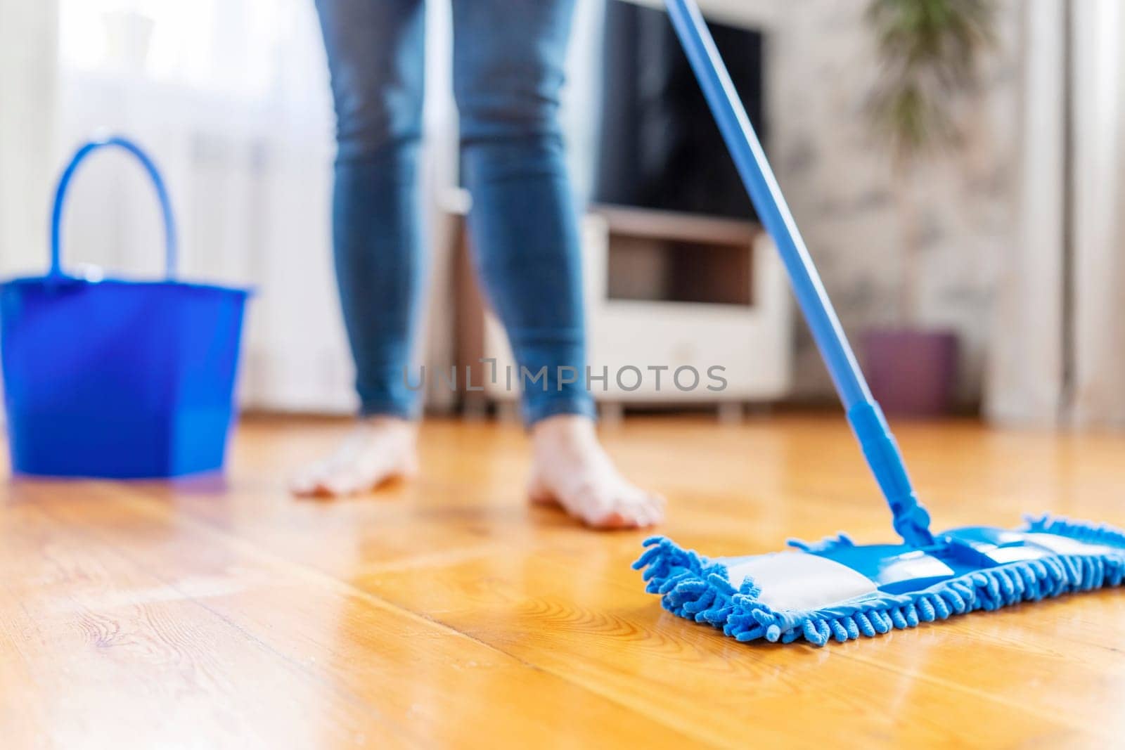 Cropped image of young woman in casual clothes washing a wooden floor with a damp microfiber mop, doing homework, routine cleaning, cleaning job concept