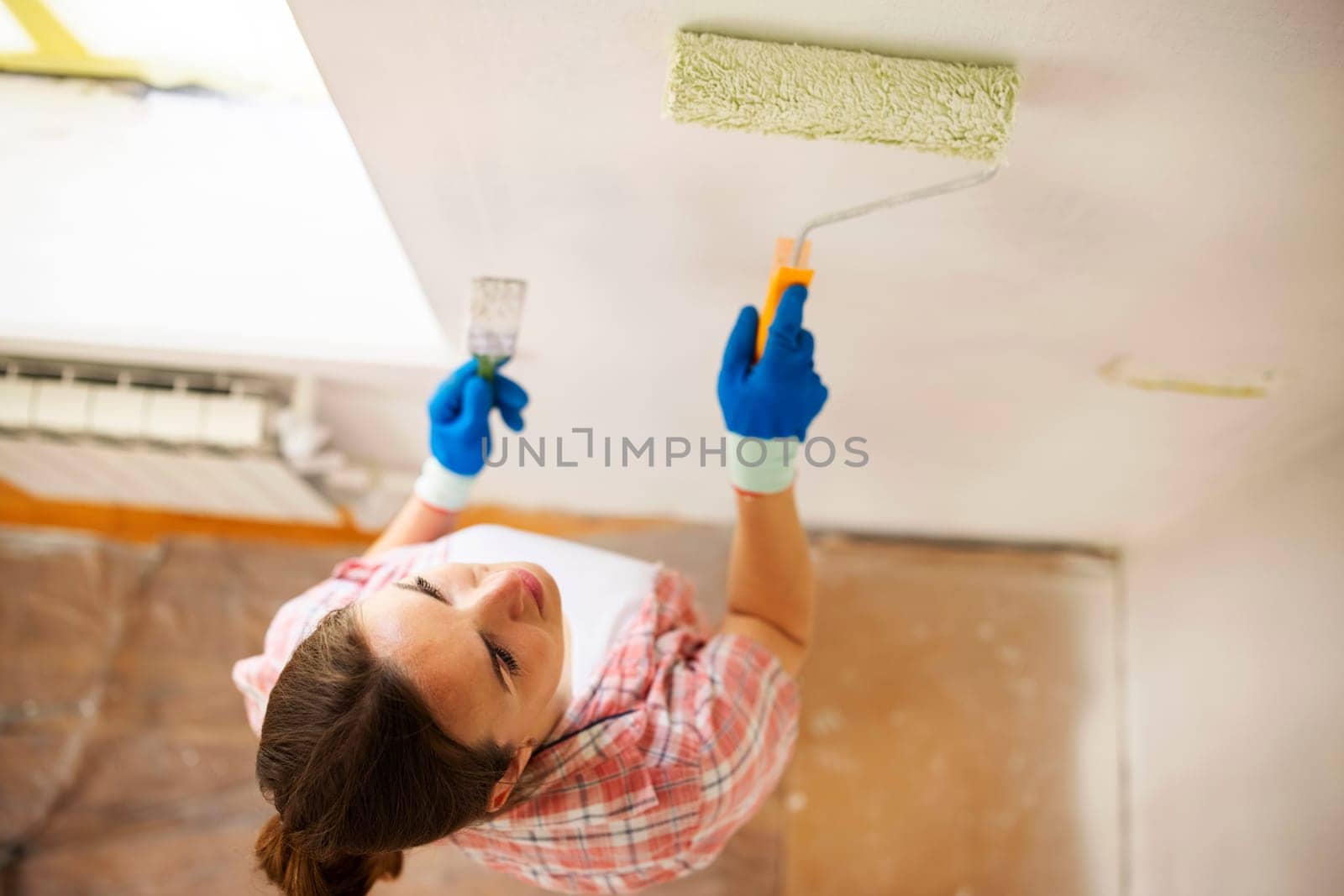 Happy woman with roller painting wall in her new apartment. Renovation, redecoration and repair concept