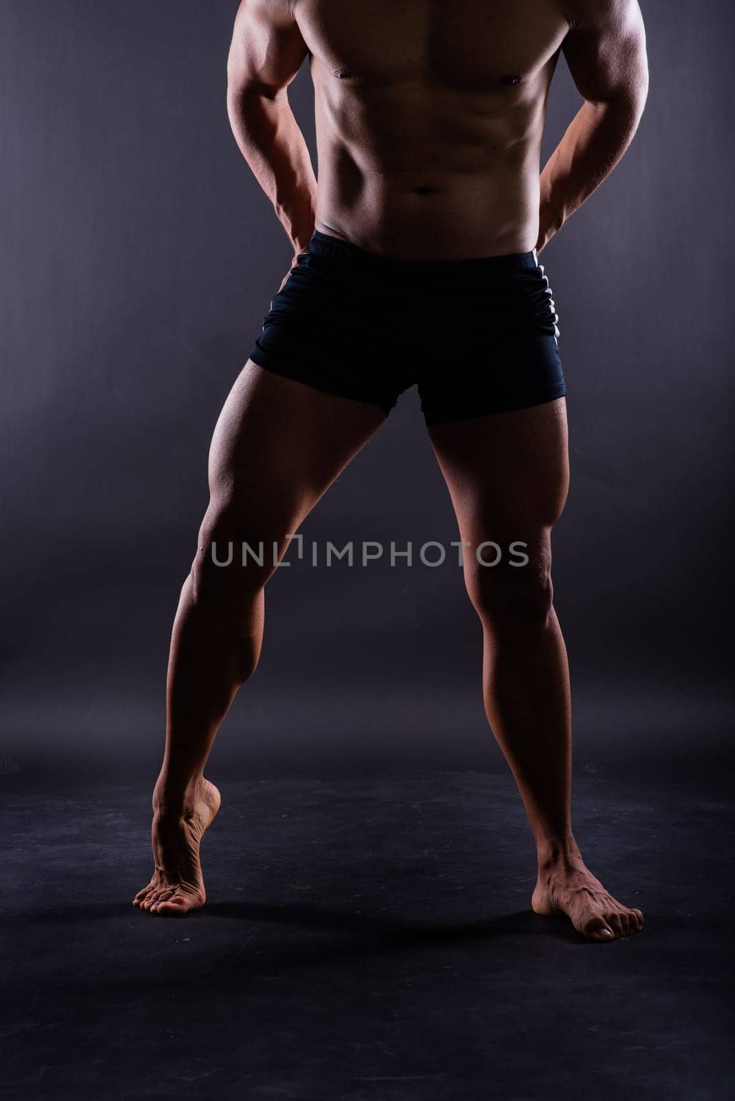 Muscular male legs, man in a studio, dark background