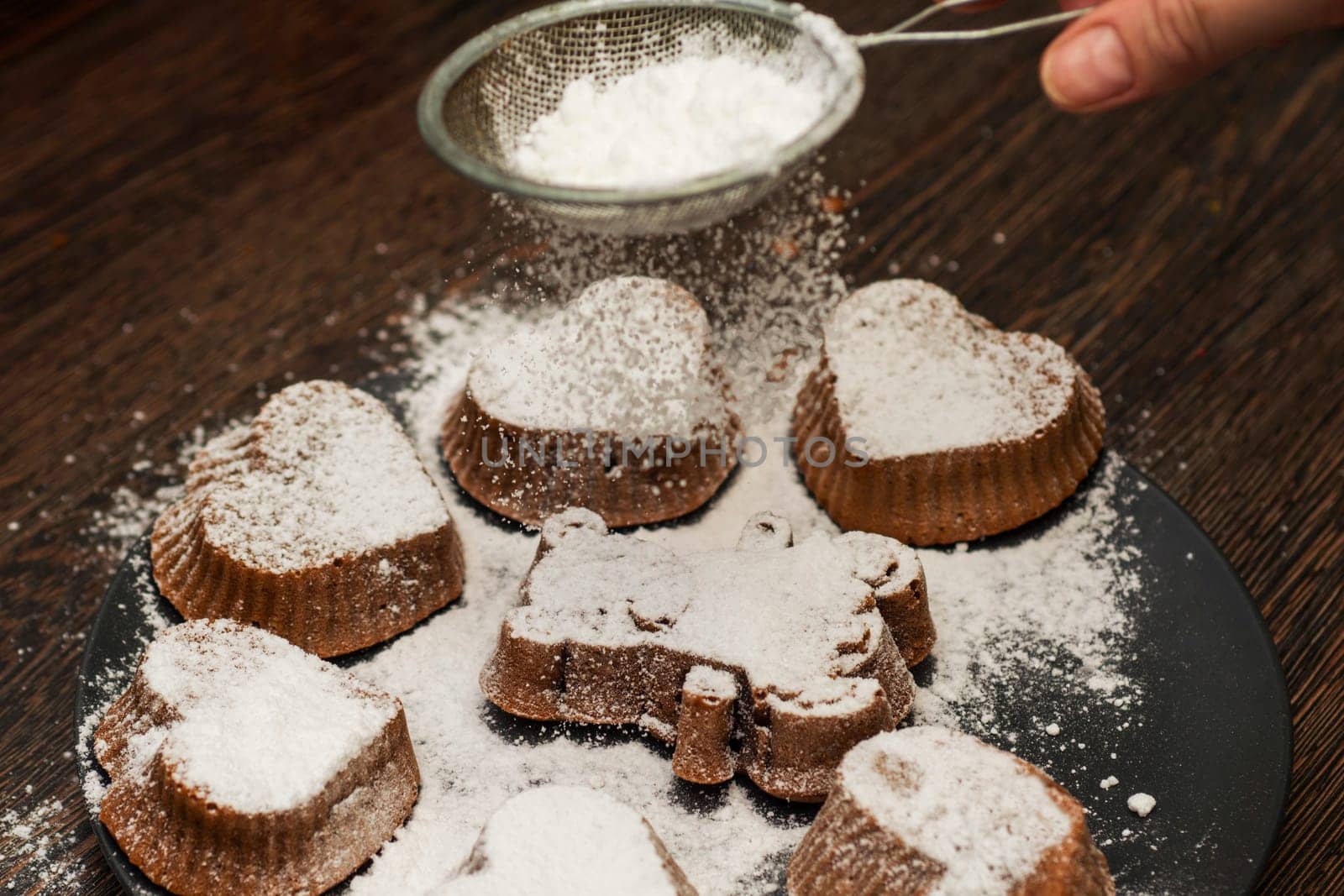 Woman's hand sprinkle icing sugar over fresh muffinsor cupcakes. Homemade bakery.