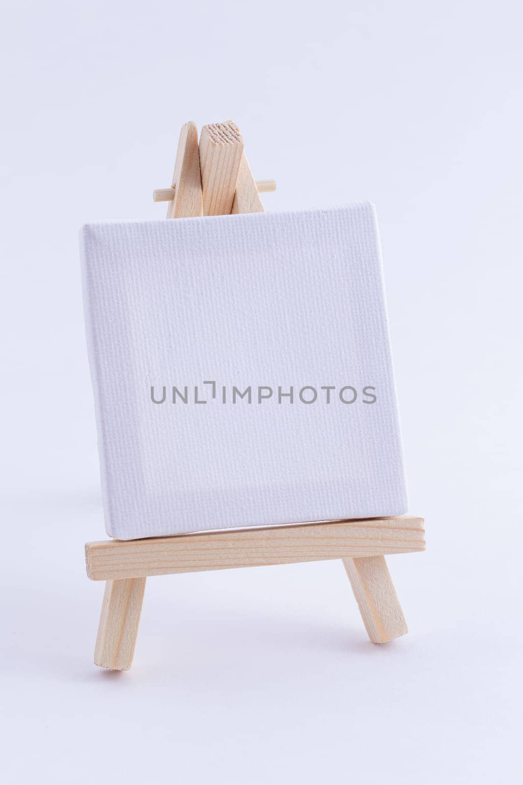 Wooden Easel Miniature with Blank White Square Canvas for Artists and Painters - Mockup. Mini Wooden Stand with Clean Artboard on White Background, Copy Space