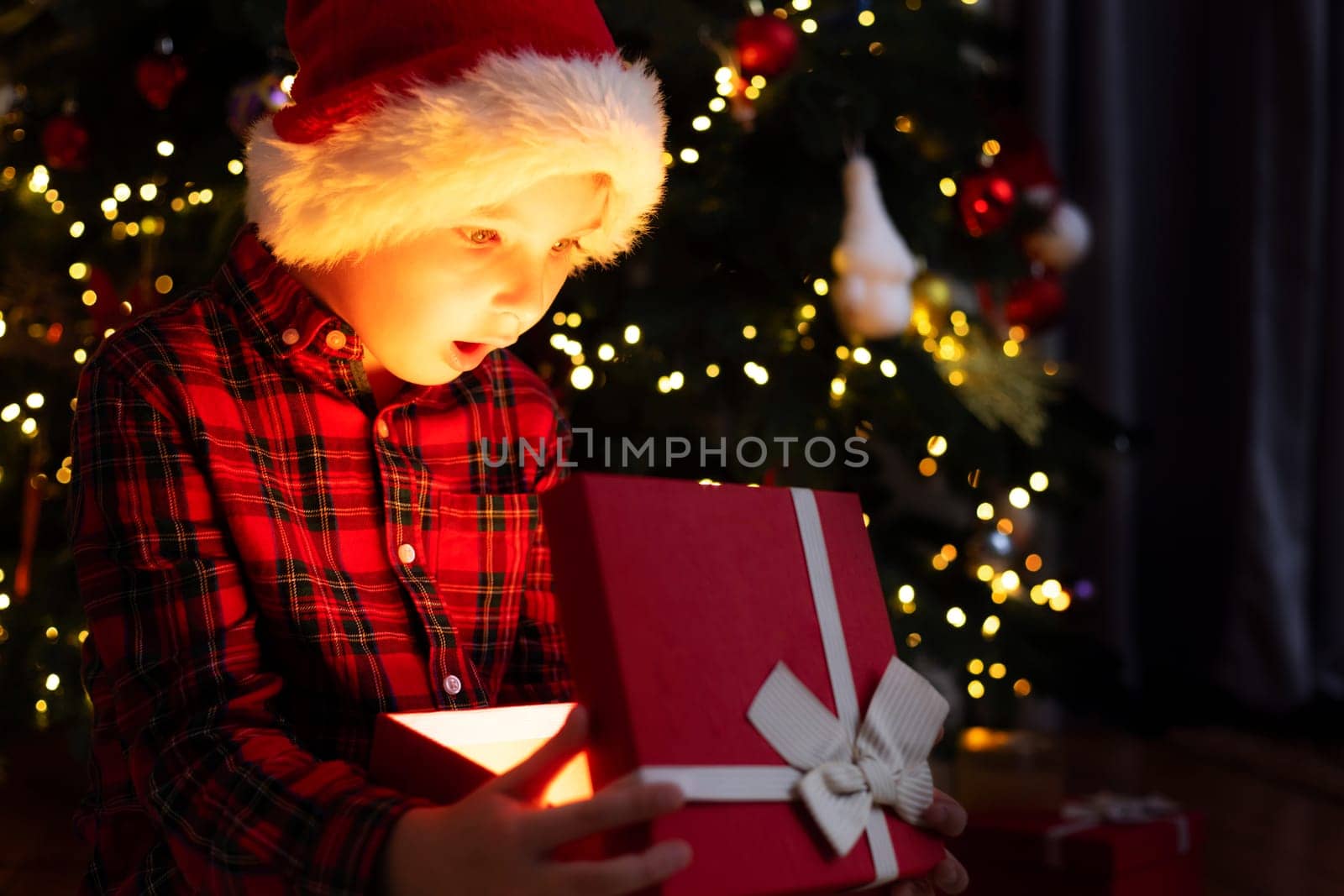 Cute little boy opening magic Christmas gift by a Christmas tree in cozy living room in winter. Merry Christmas