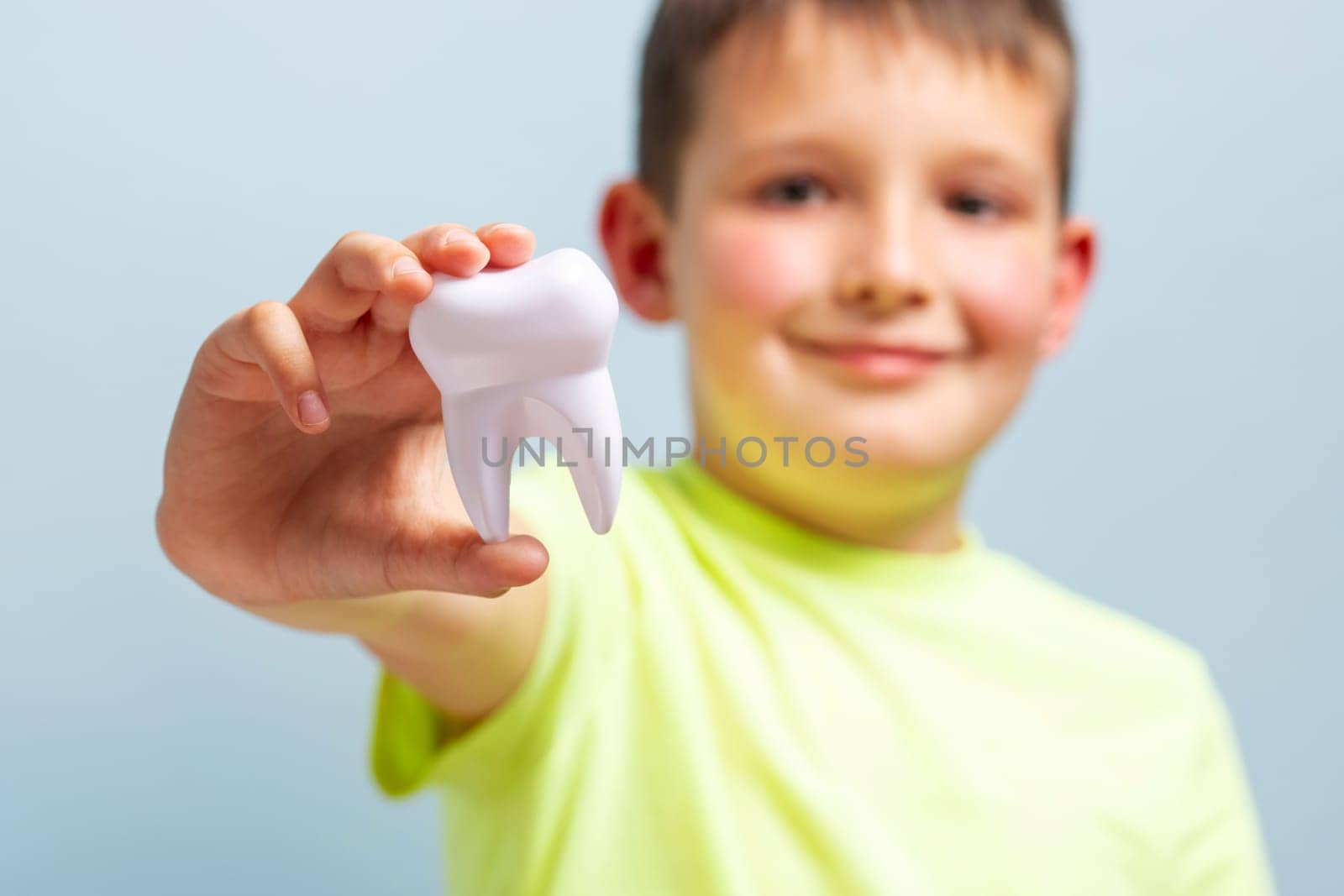 Child holds big white toy tooth on a blue background. Caring for teeth by andreyz