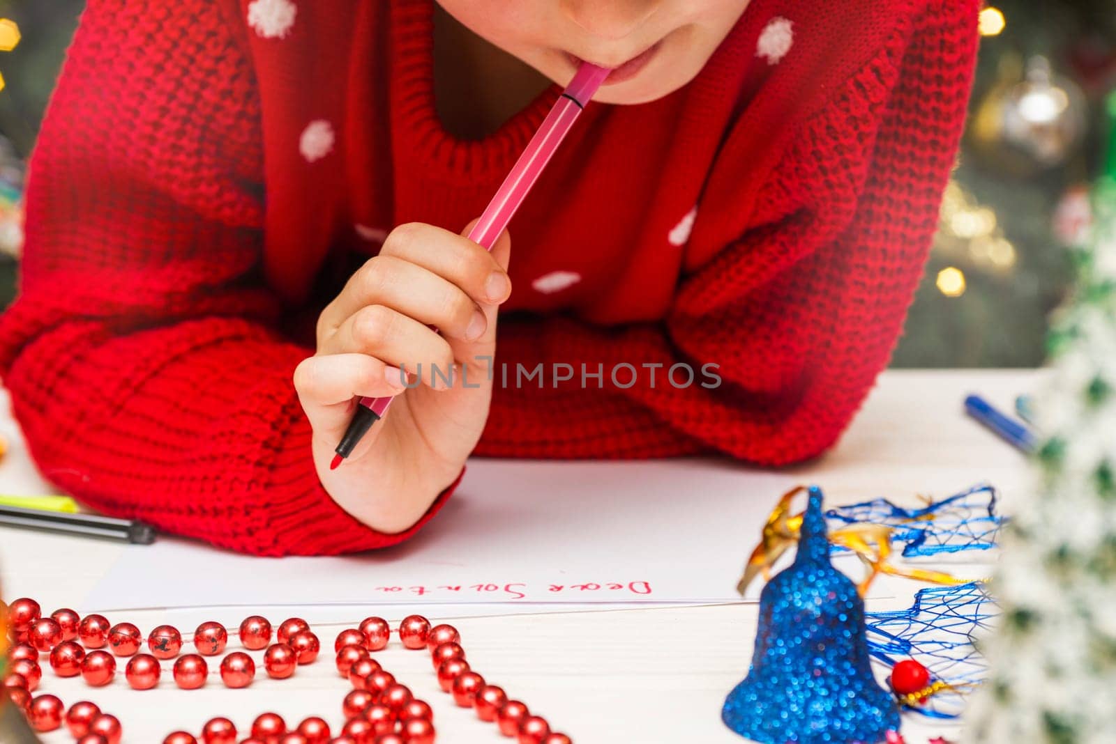Little boy in a red sweater writes letter to Santa Claus. Christmas Child writing wish list.