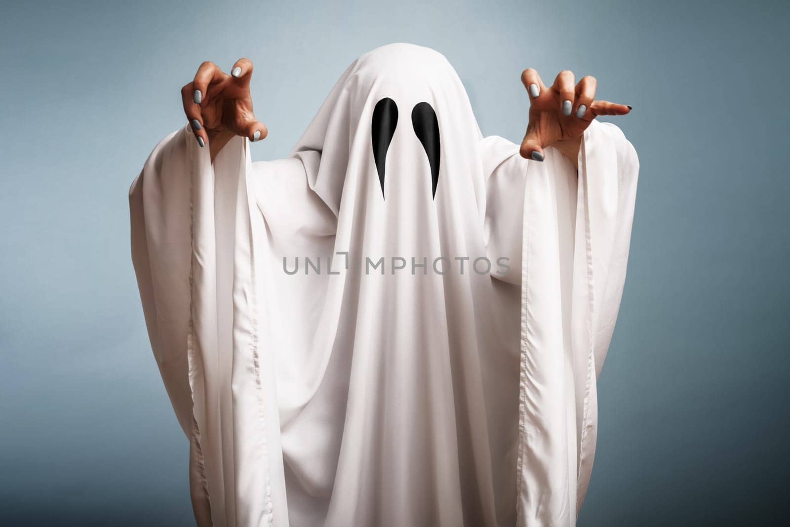 Halloween Concept. A white ghost with black eyes, made from a bedsheet on blue background.
