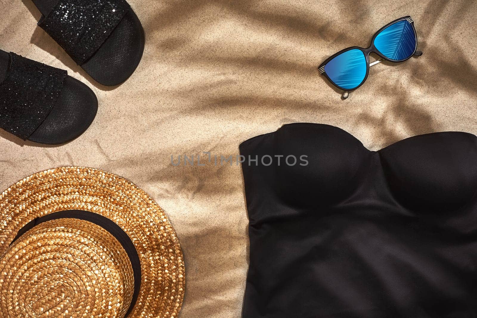 Women's beach accessories or summer outfit on sand background. Shadow from a palm leaf. Top view. Still life. Copy space. Flat lay