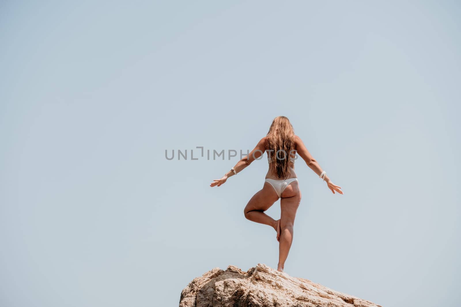 Woman sea yoga. Back view of free calm bliss satisfied woman with long hair standing on top rock with yoga position against of sky by the sea. Healthy lifestyle outdoors in nature, fitness concept. by panophotograph